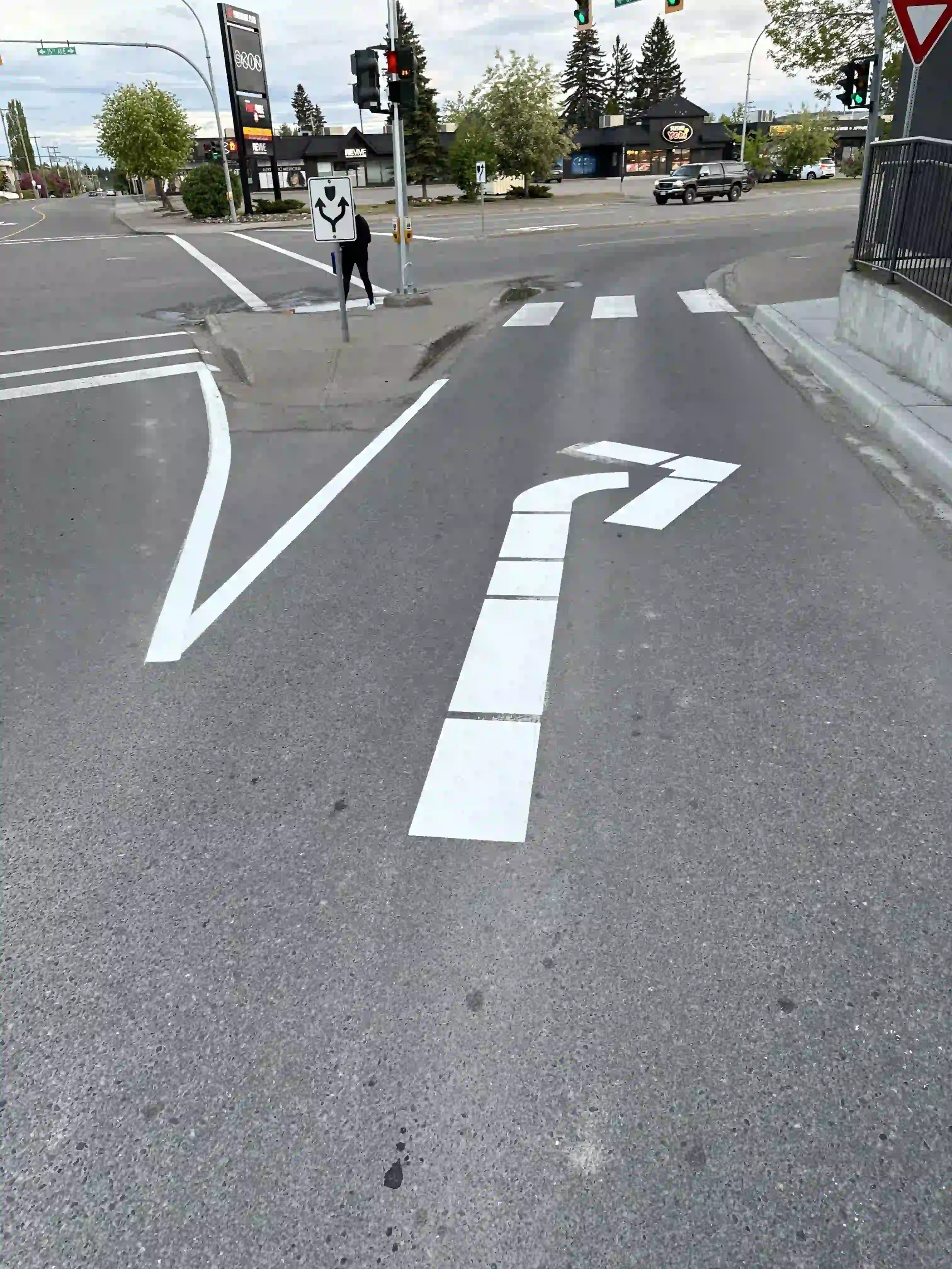 Roadway line painting and white turn arrow pavement markings at a commercial plaza entrance in Terrace, BC.