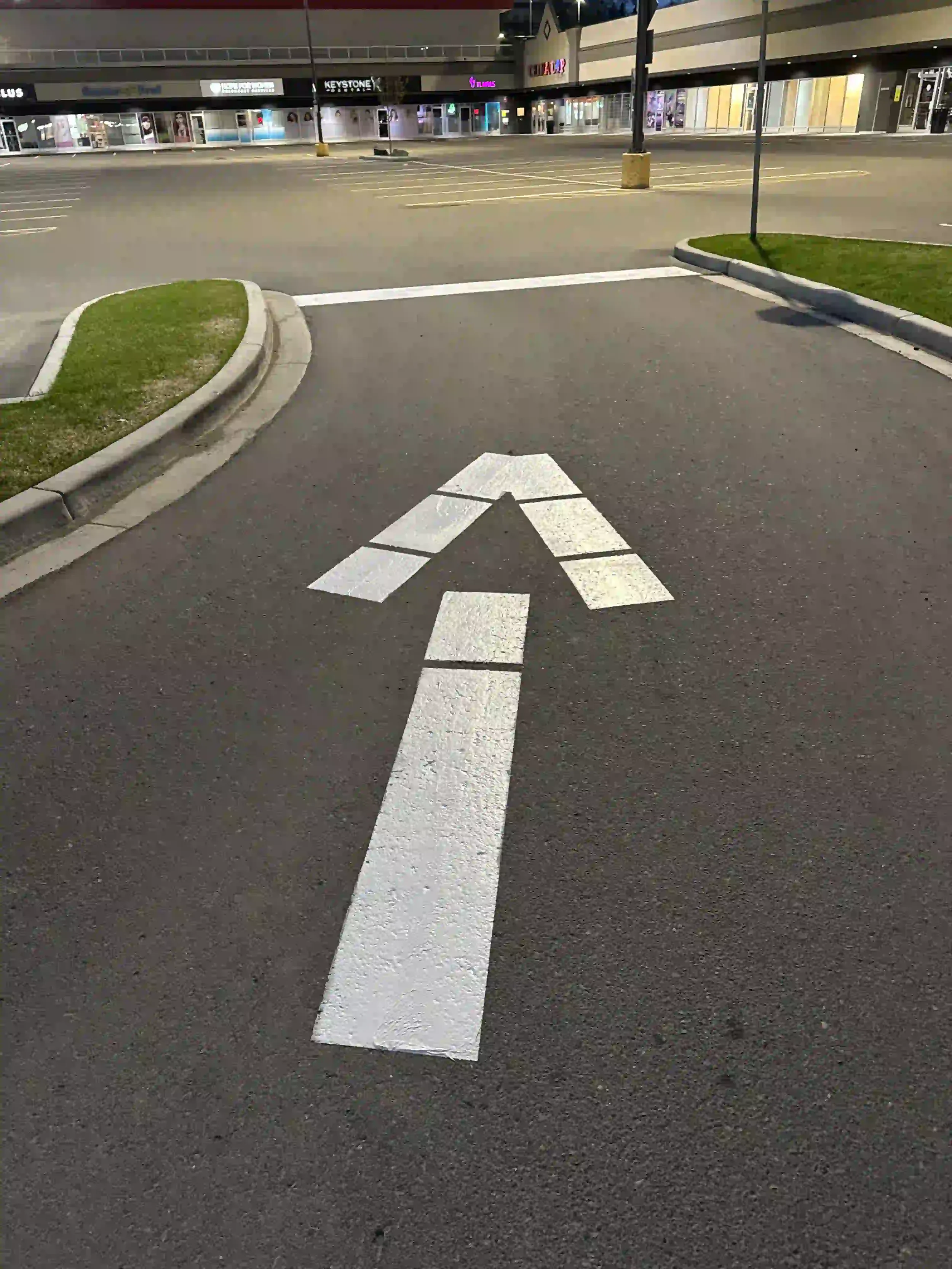 Freshly painted white directional arrow and line markings in a commercial shopping plaza parking lot in Fort St. John, BC, showcasing professional pavement marking services.