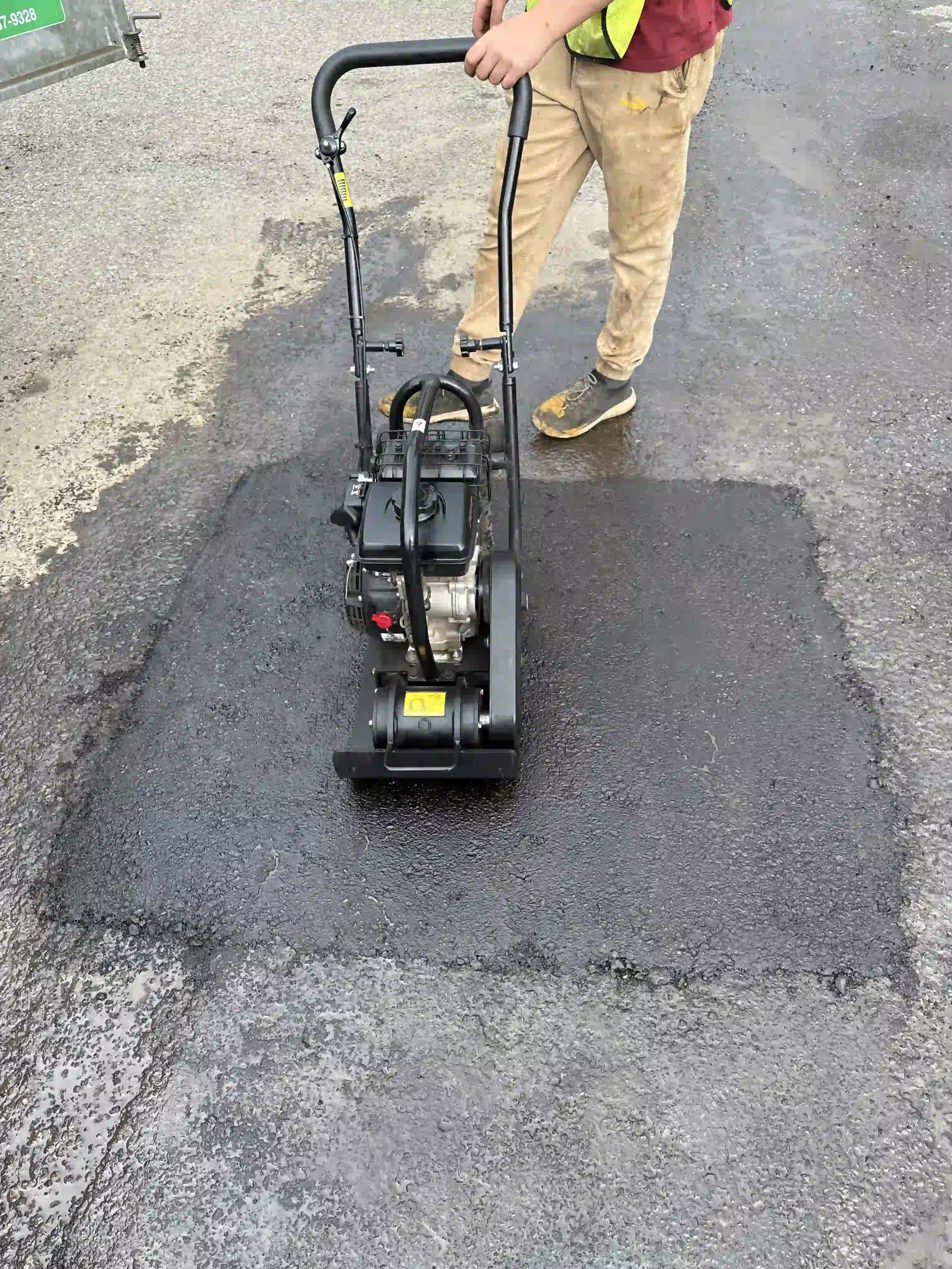 An Epic Pavement professional using a walk-behind plate compactor to finish and level a fresh asphalt patch repair on a commercial property.