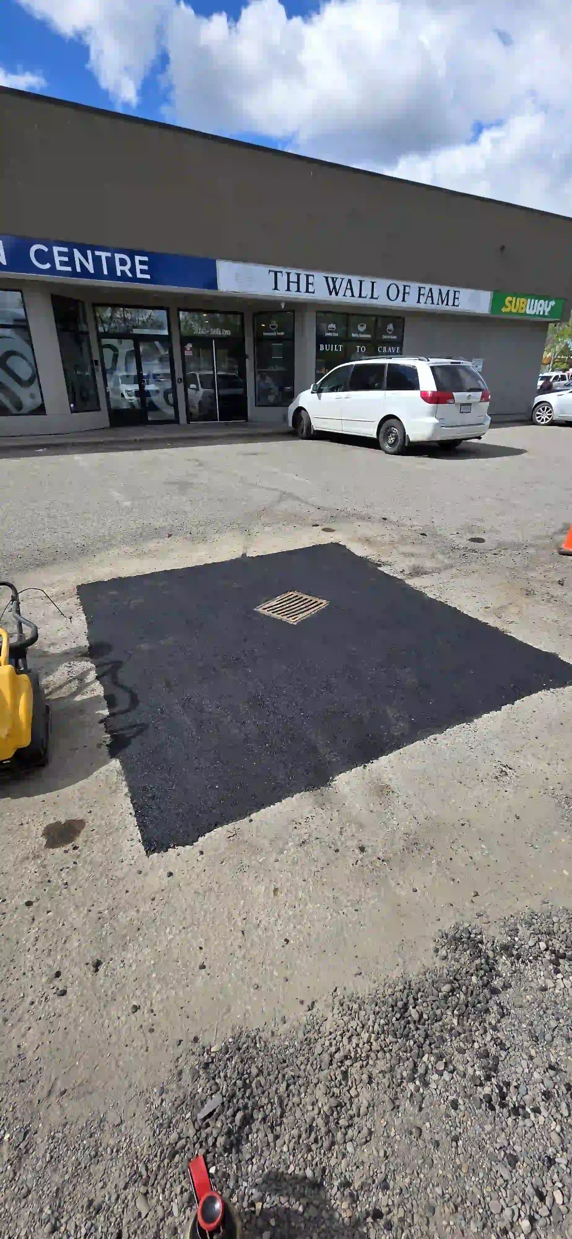 A freshly completed asphalt repair and pothole patch surrounding a catch basin, restoring safety and usability to a commercial parking lot in Prince George.