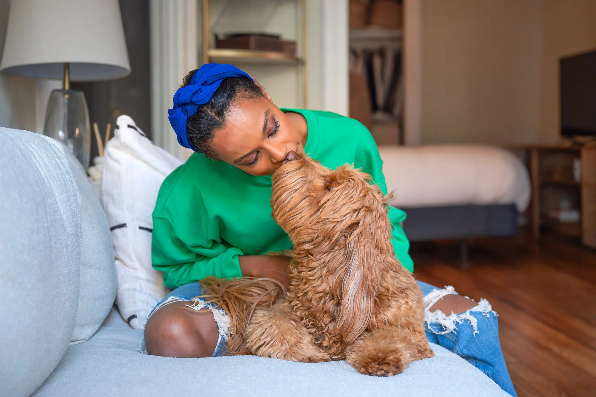 Person sitting on a sofa, lovingly interacting with a brown fluffy dog inside a cozy room.