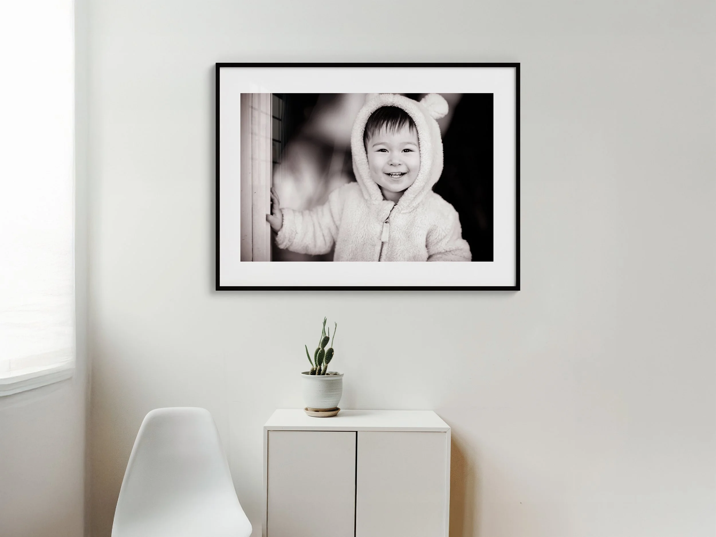 Modern bedroom with neutral colors, featuring a framed family photo above the bed, decorative vase on a side table, and a lamp on the other side.