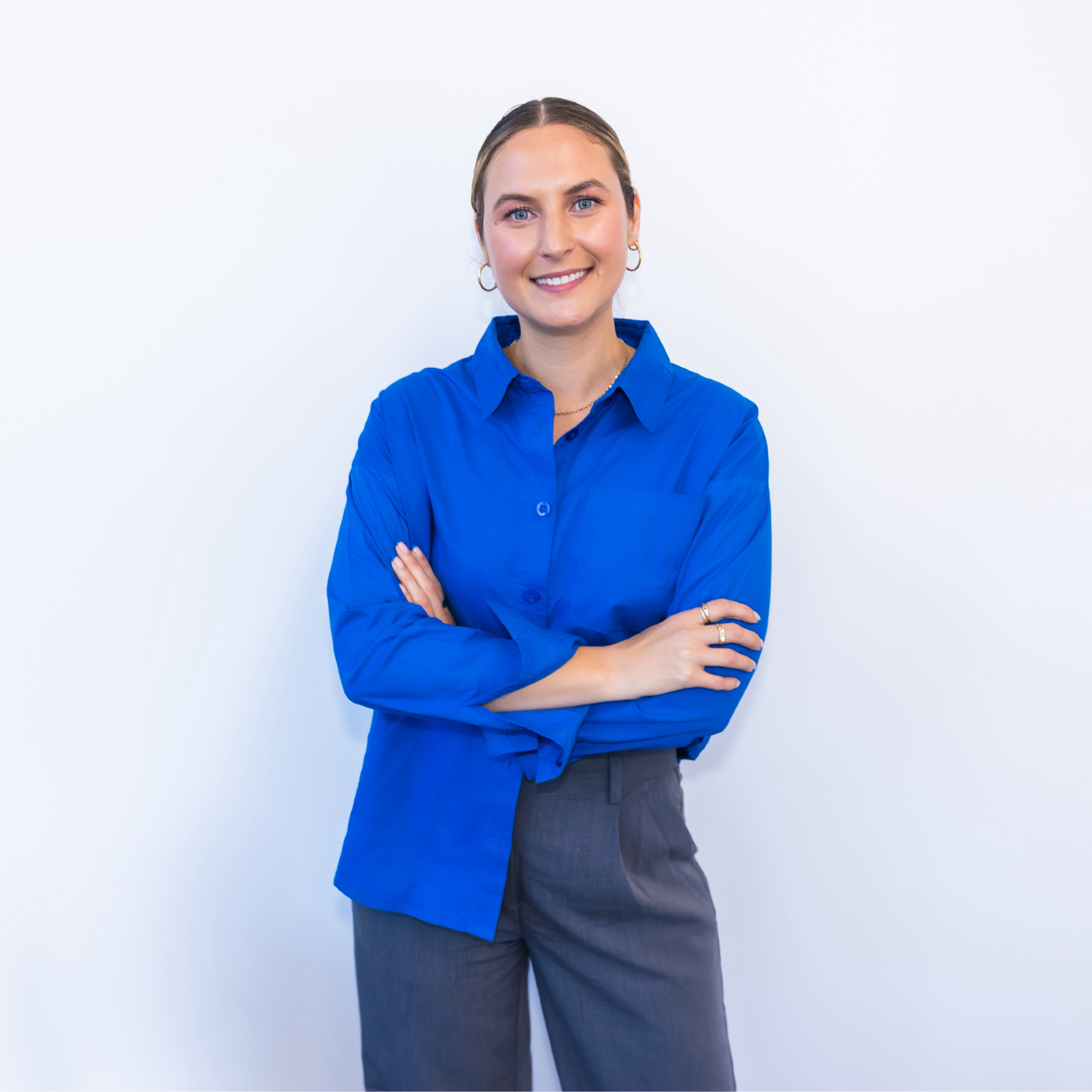 Jess Diakoumakos, Melbourne naturopath and founder of Emba Wellness, providing personalised, evidence-based care with pathology interpretation, she is wearing a blue shirt with grey pants and smiling