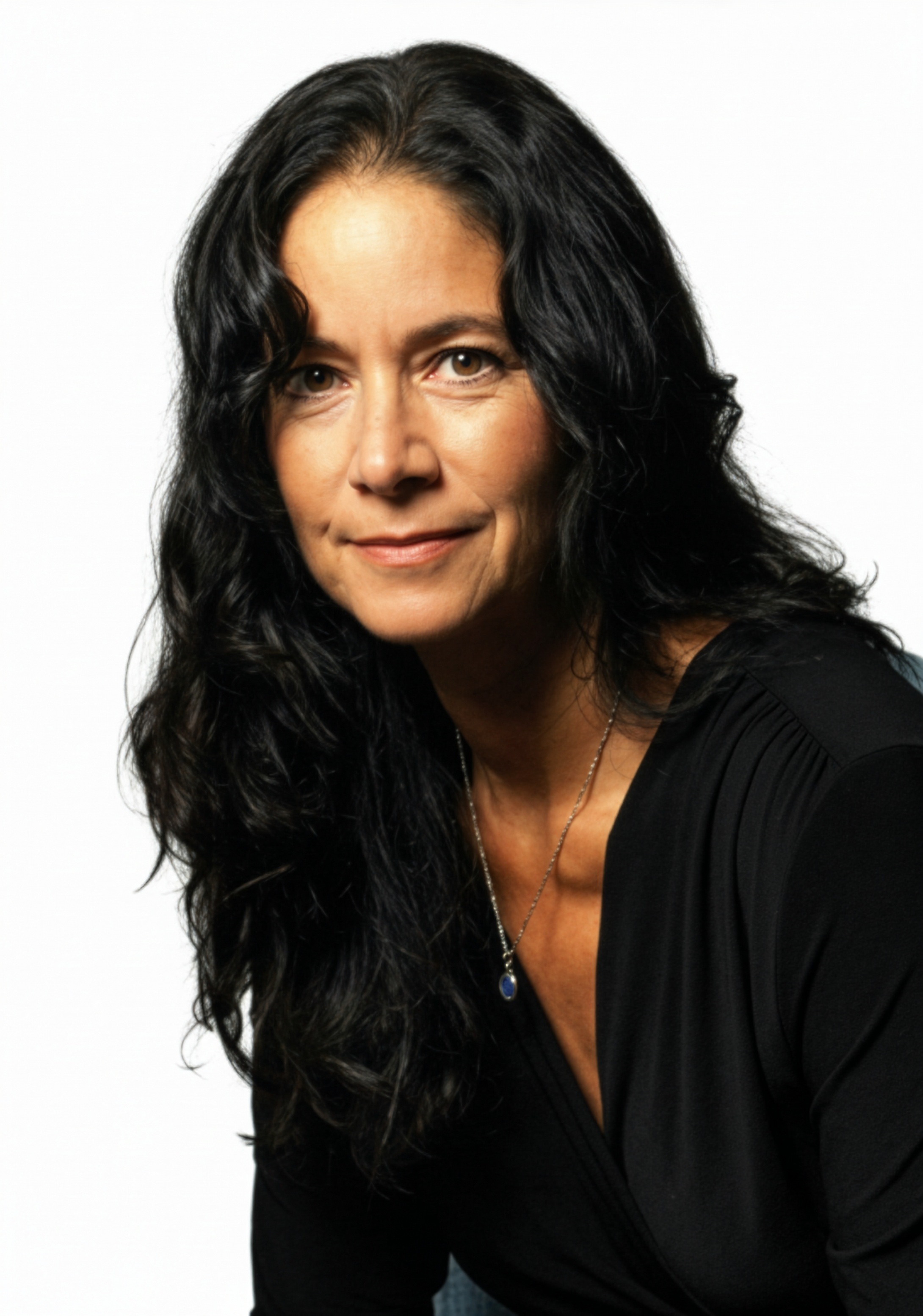 Portrait of a woman with long black curly hair, wearing a black top and a silver necklace with a blue pendant, against a white background.