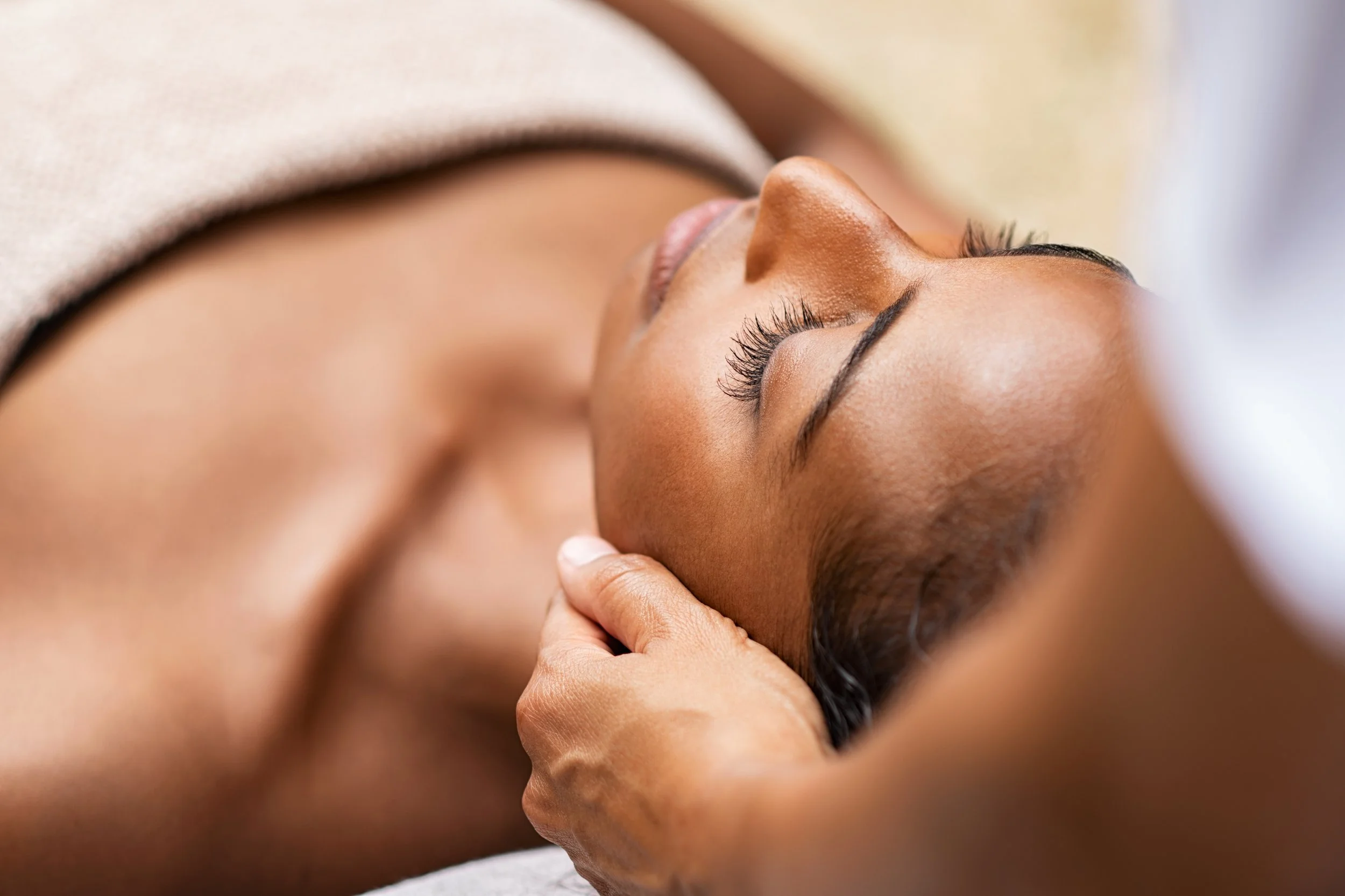 Close-up of a woman receiving a massage on her face with her eyes closed.