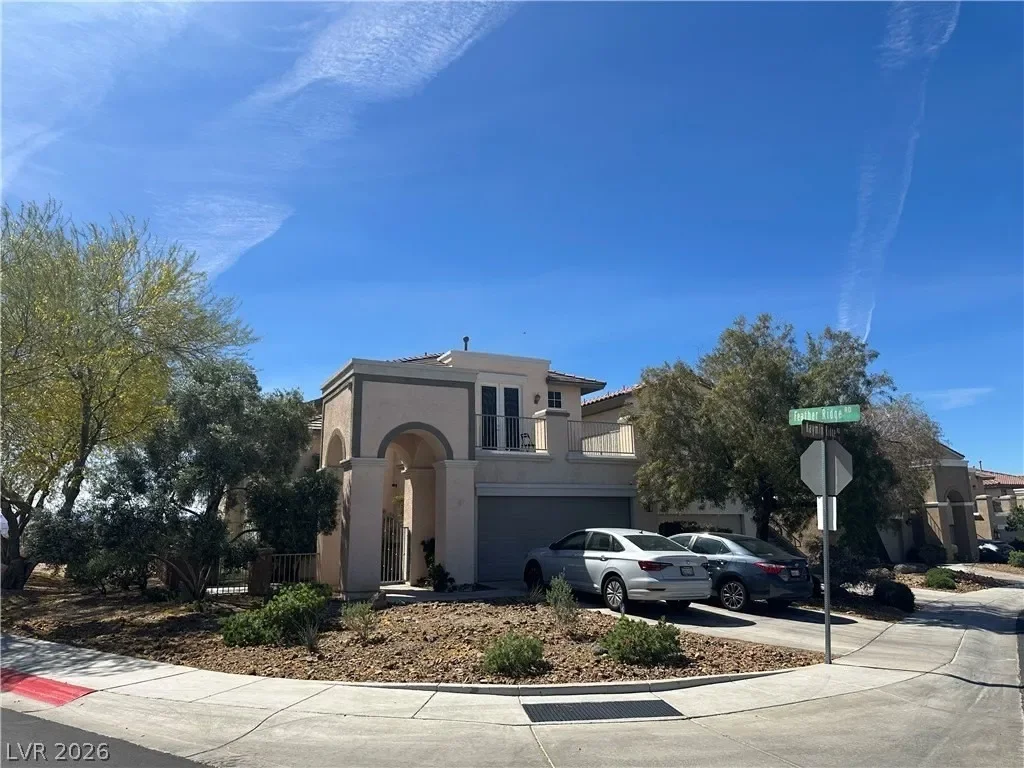 Exterior view of a two-story home for sale in Henderson, Nevada featuring a stucco facade, arched entryway, two-car garage, and desert landscaping on a corner lot under a clear blue sky.