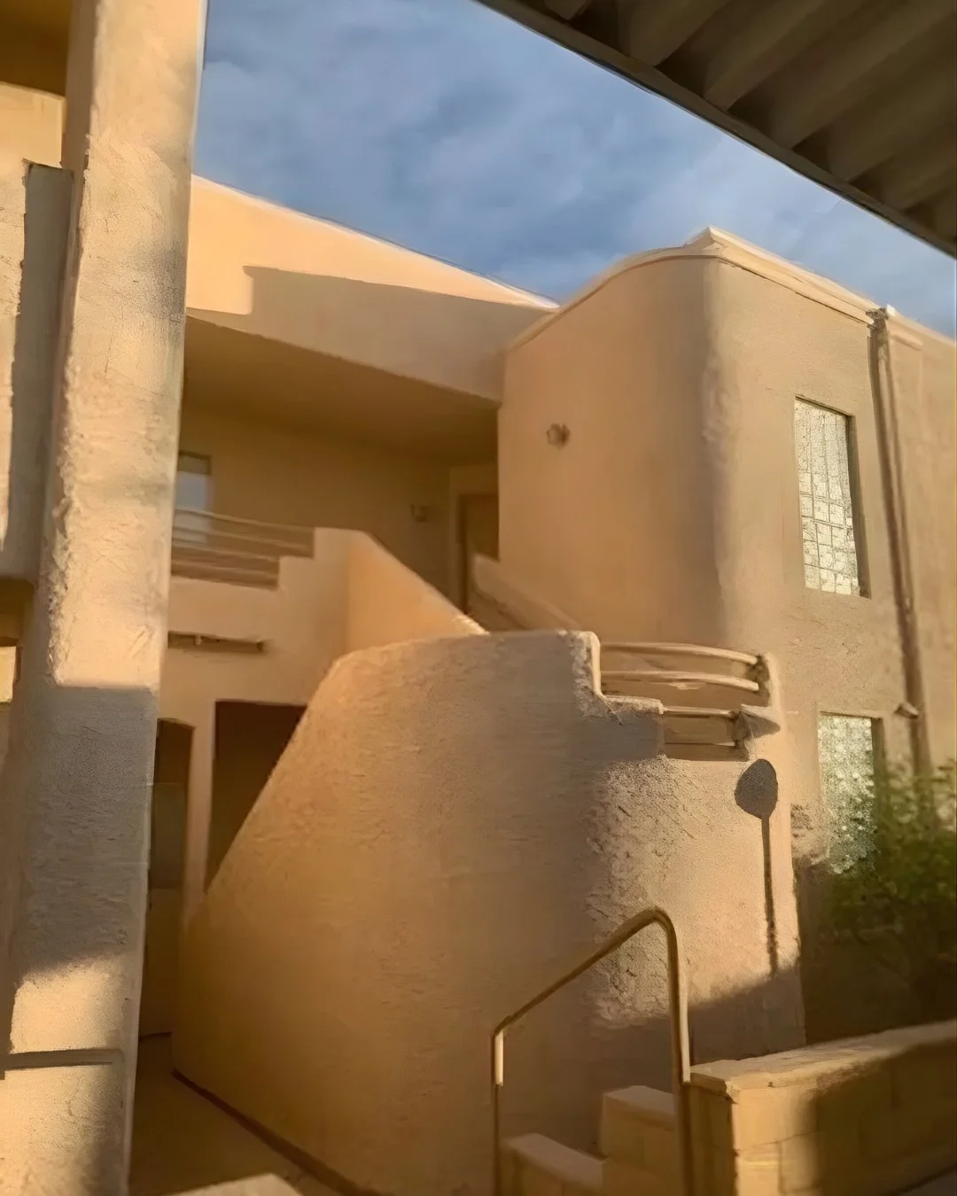Exterior view of a stucco condo building in Laughlin, Nevada featuring a staircase entry, covered walkway, and warm natural lighting in a quiet residential community.