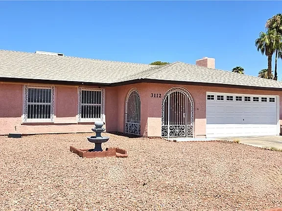 Exterior view of the single-story home at 3112 Elmrock Place in Las Vegas, featuring a pink stucco façade, decorative security gates, a two-car garage, and low-maintenance desert landscaping.