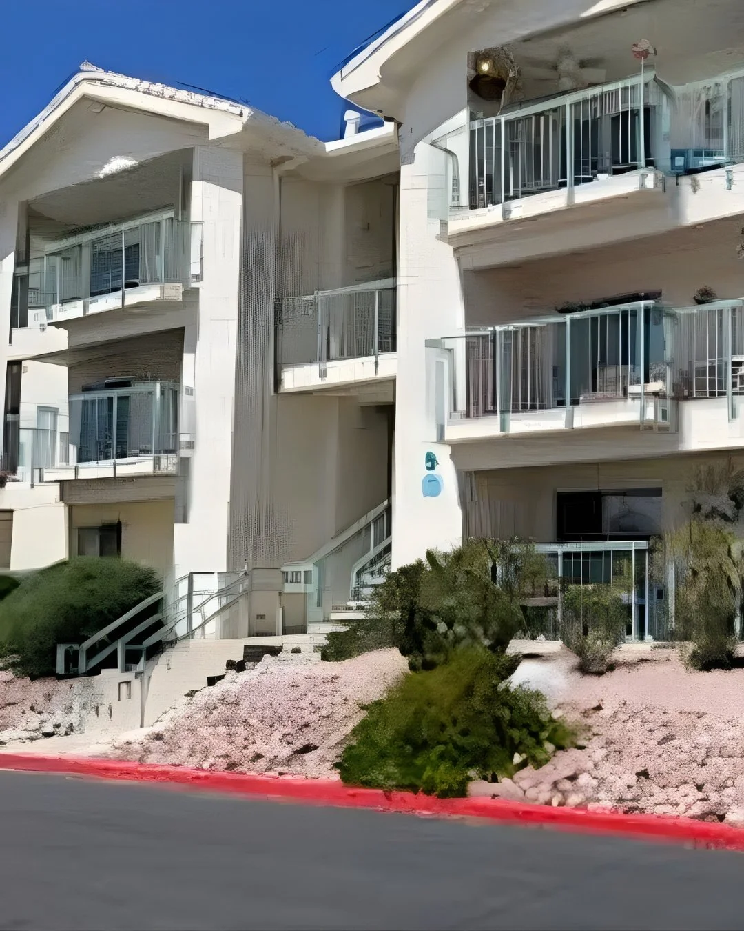 Exterior view of a multi-level condo building in Laughlin, Nevada featuring white stucco architecture, private balconies, desert landscaping, and a well-maintained community setting under a clear blue sky.