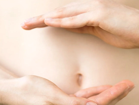 Close-up of a person's bare torso with hands forming a rectangle around the navel.