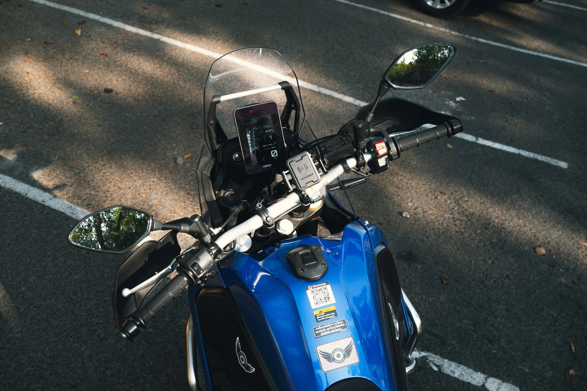 Top view of a blue motorcycle parked in a parking lot with white lines and fallen leaves on the asphalt.