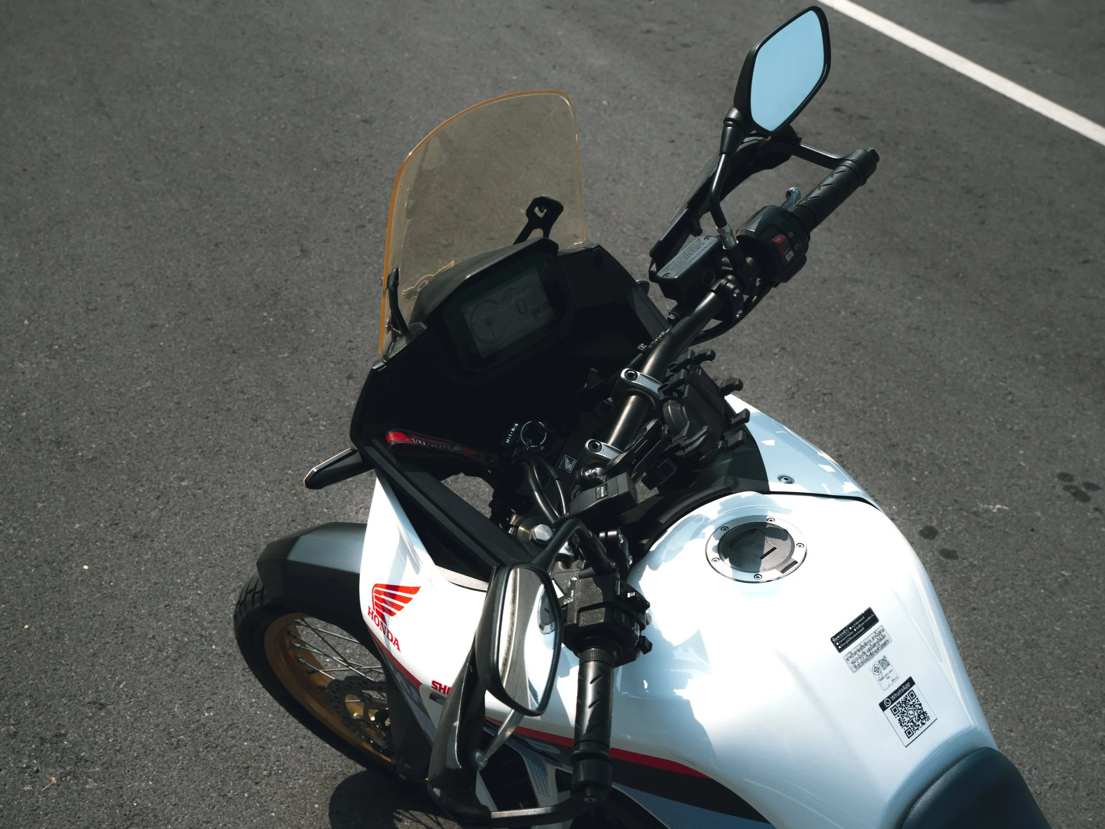Top view of a white Honda motorcycle with a yellow windshield on a gray asphalt road.