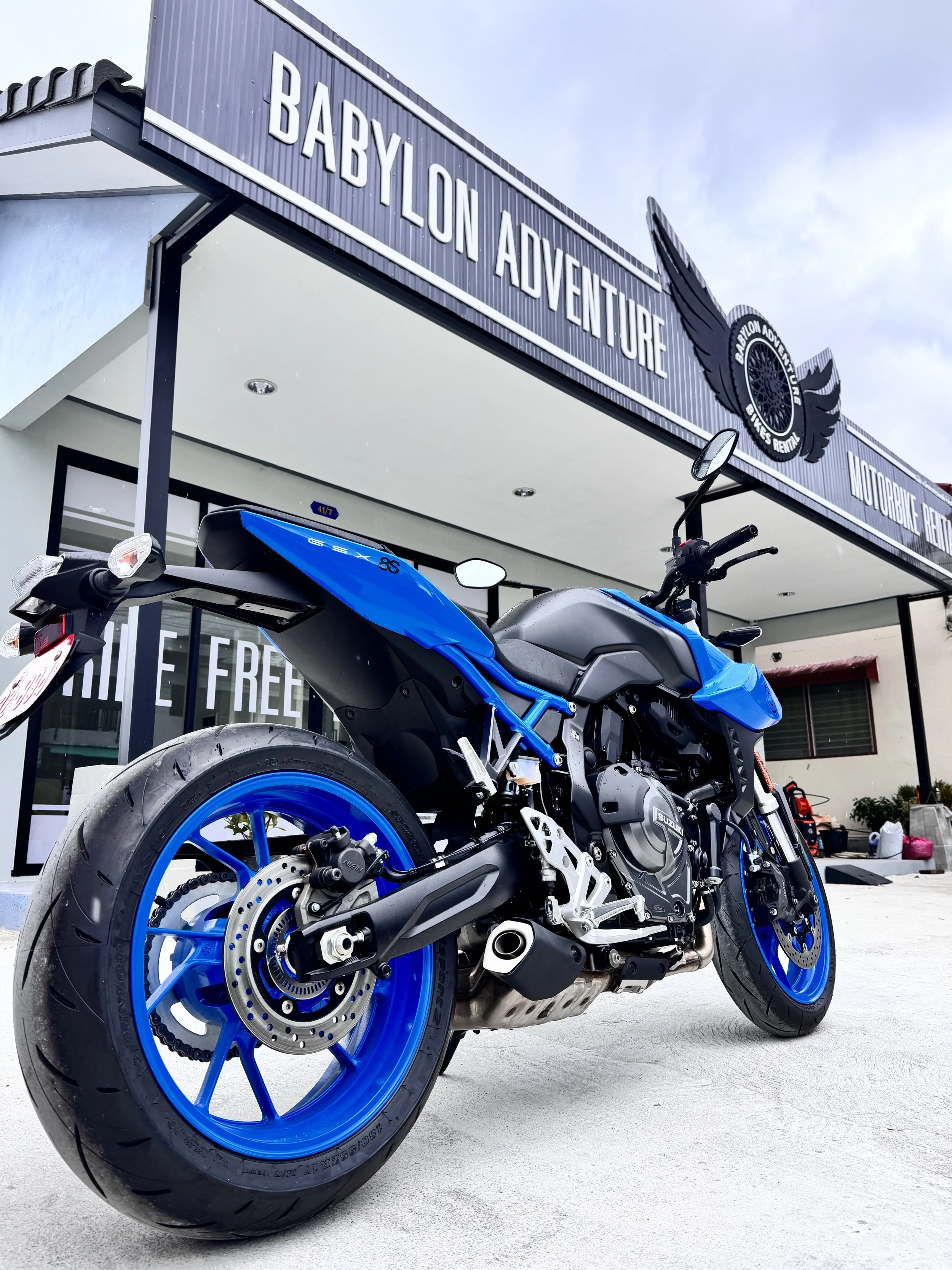 A blue motorcycle parked outside Babylon Adventure motorbike rental shop.