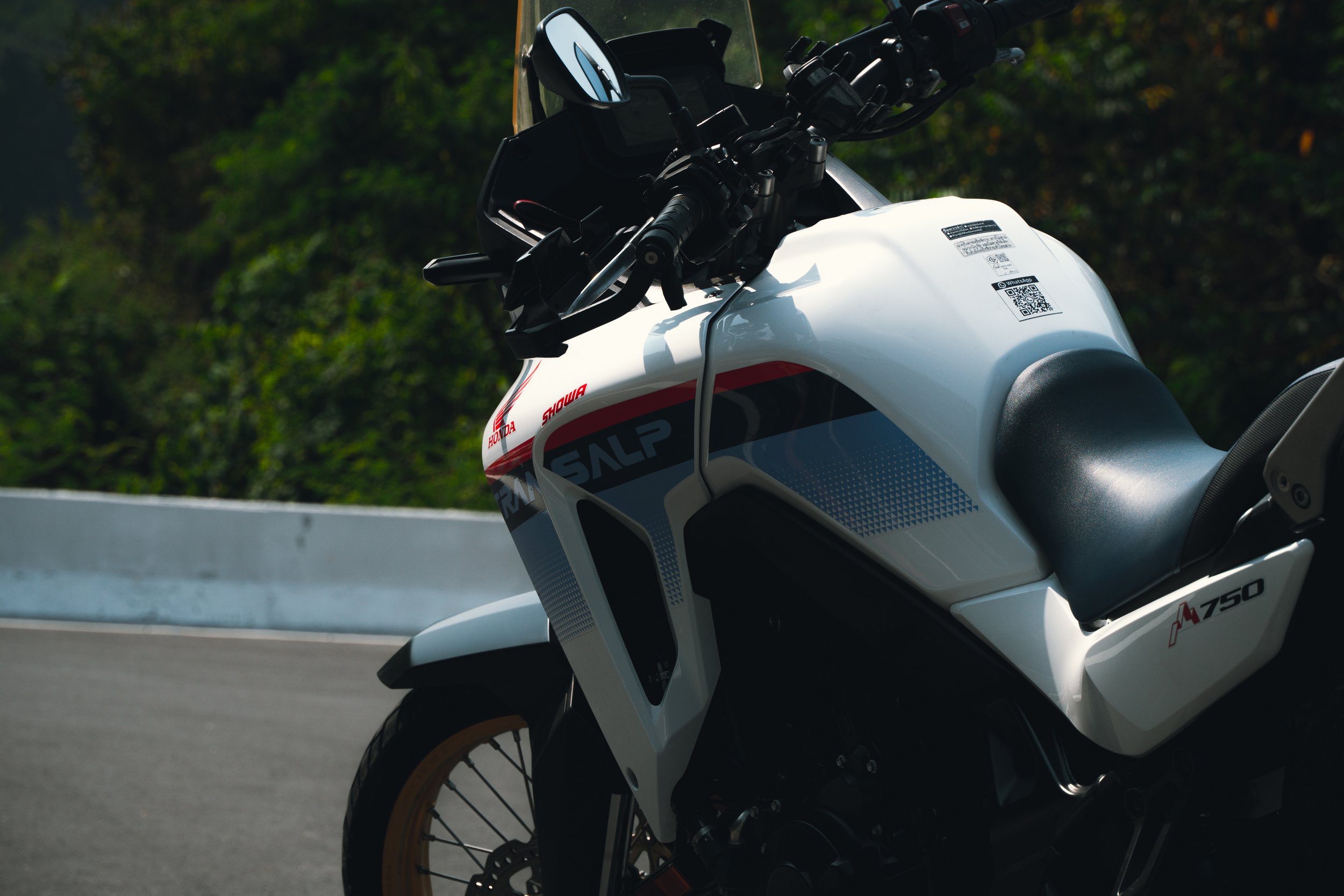 Close-up of a white Honda motorcycle parked on the side of a road with trees in the background.