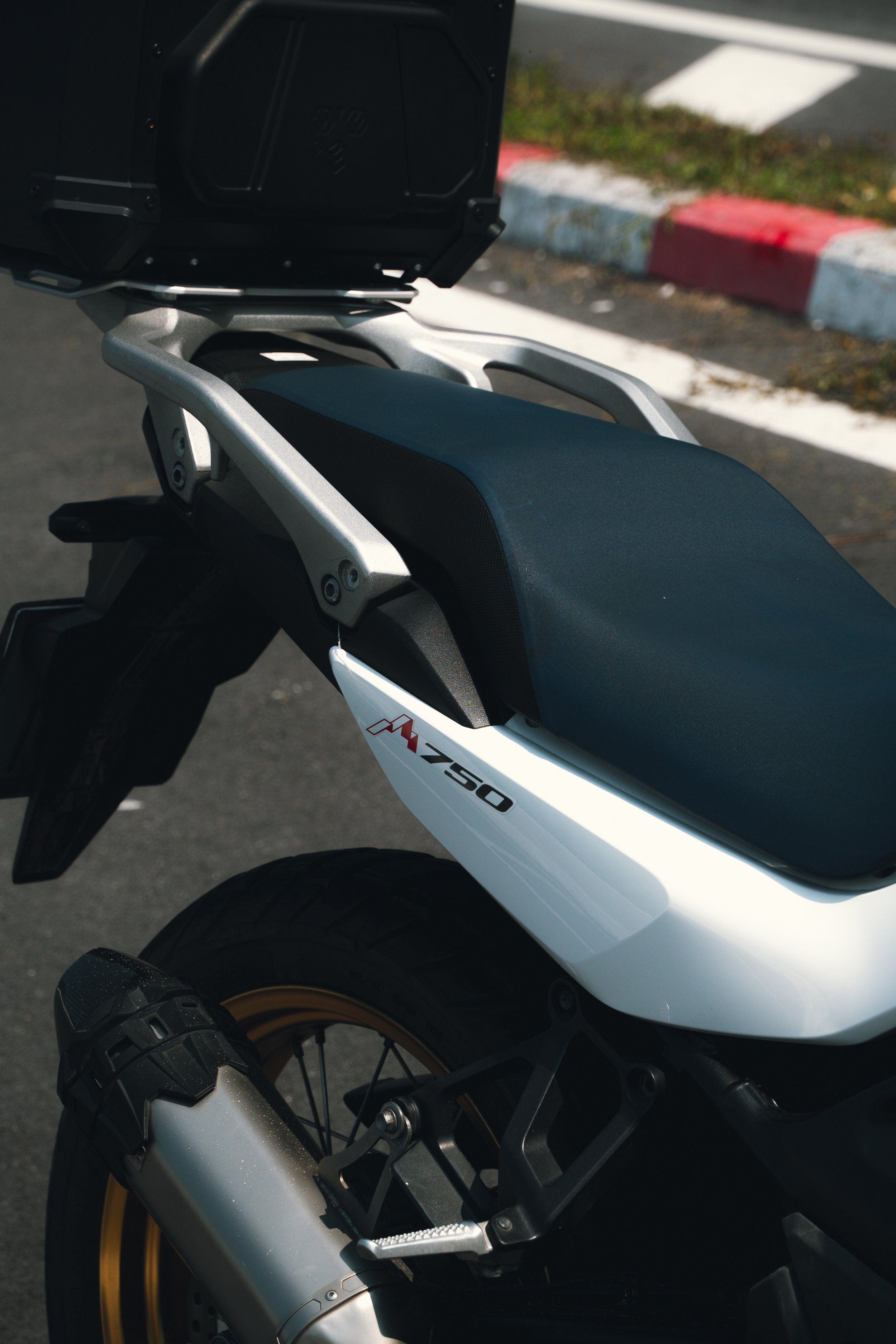 Close-up of a white Honda Africa Twin motorcycle with a black seat, parked on a street near a curb painted red and white.