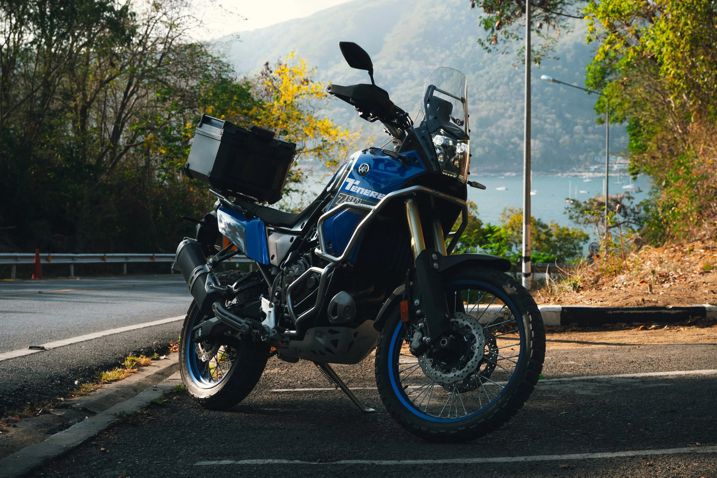 A Yamaha Teneré off-road motorcycle parked on the side of a scenic road with a lake and mountains in the background.