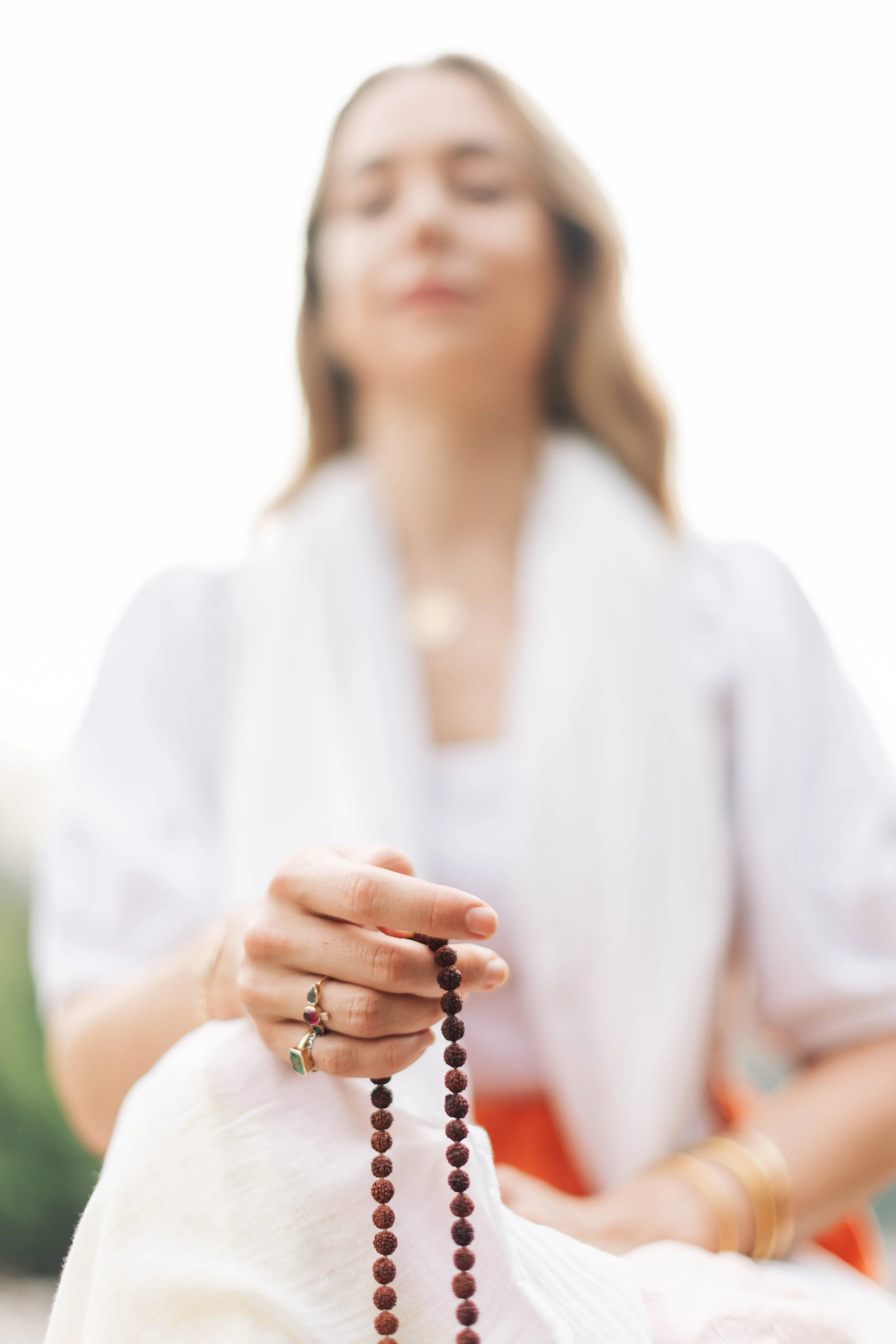 Femme tenant un mala, portant des bijoux, avec un fond lumineux et flou.