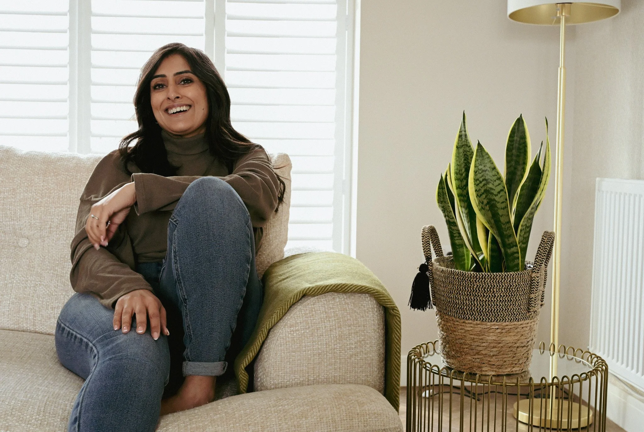 Lady sat on sofa with one leg bent with a big smile