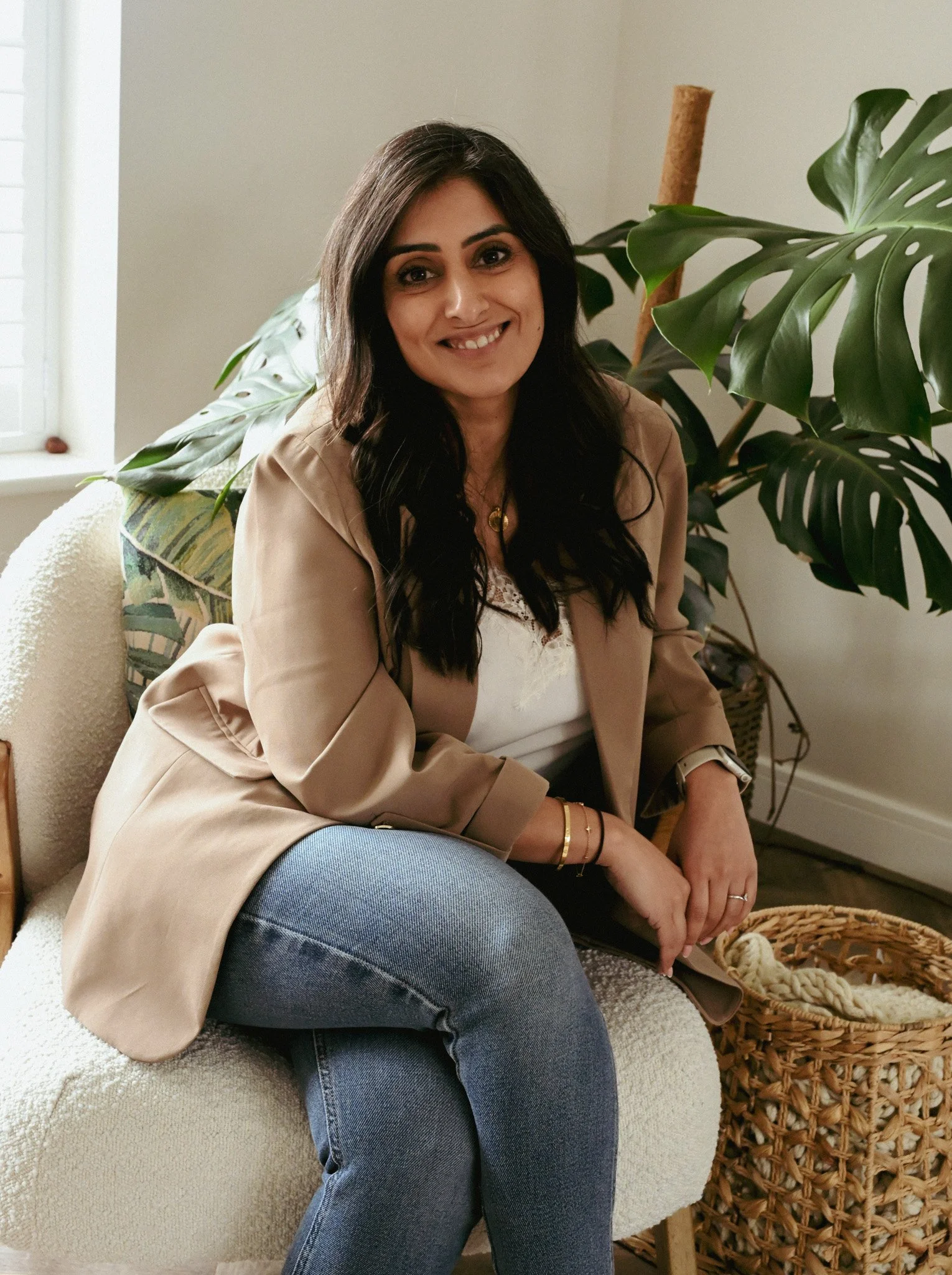 Lady sat on a chair smiling with a plant behind her