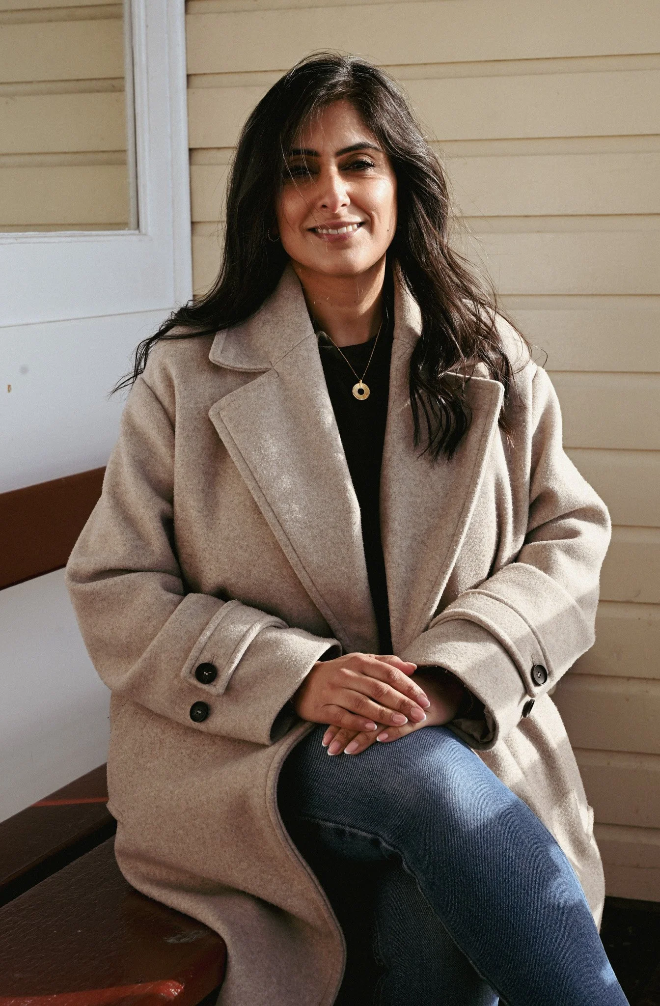 Lady sat on a bench by the beach with the sun on her face