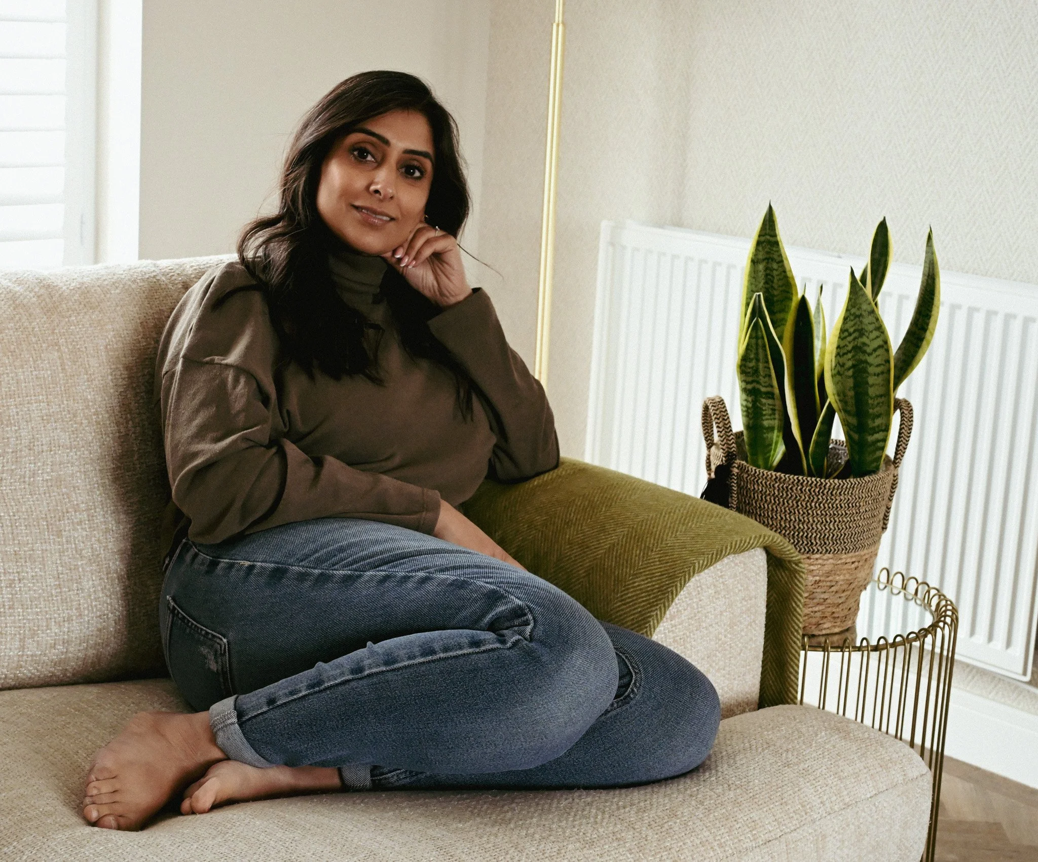 Lady sat on sofa with head resting on her hand, smiling
