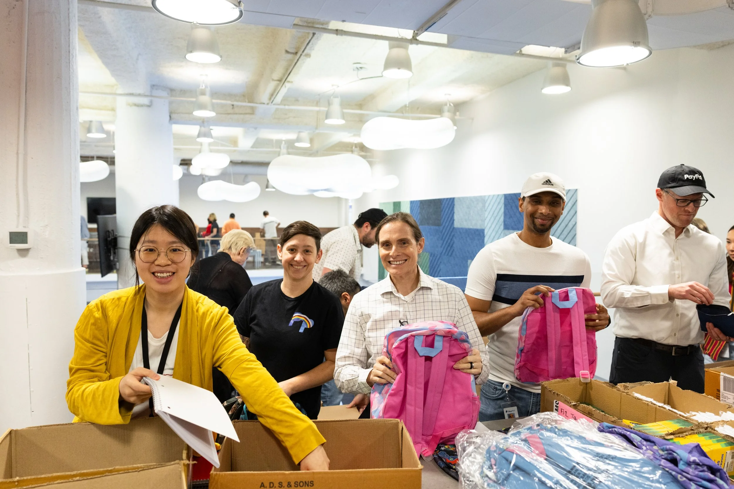 five people on a backpack assembly line stuffing backpacks