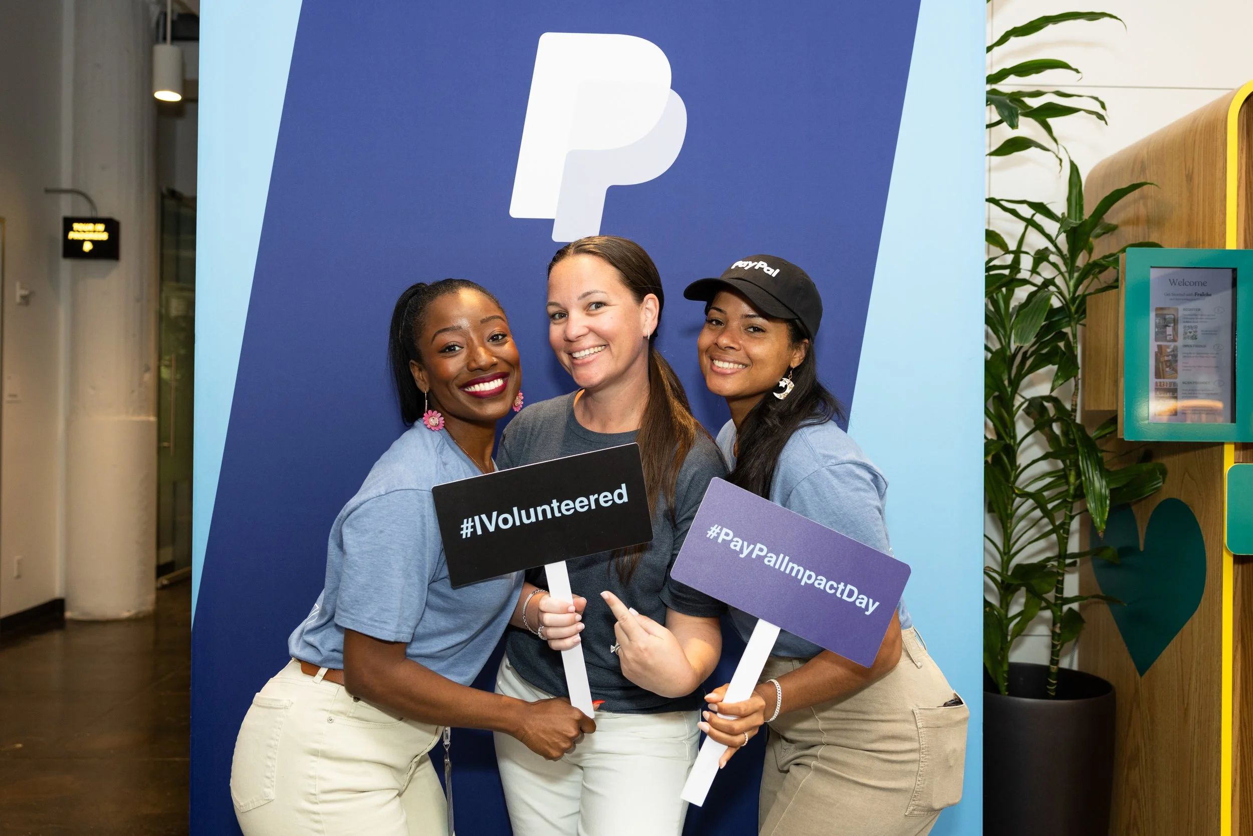 three women standing in front of a branded sign that says I volunteered smiling at the camera