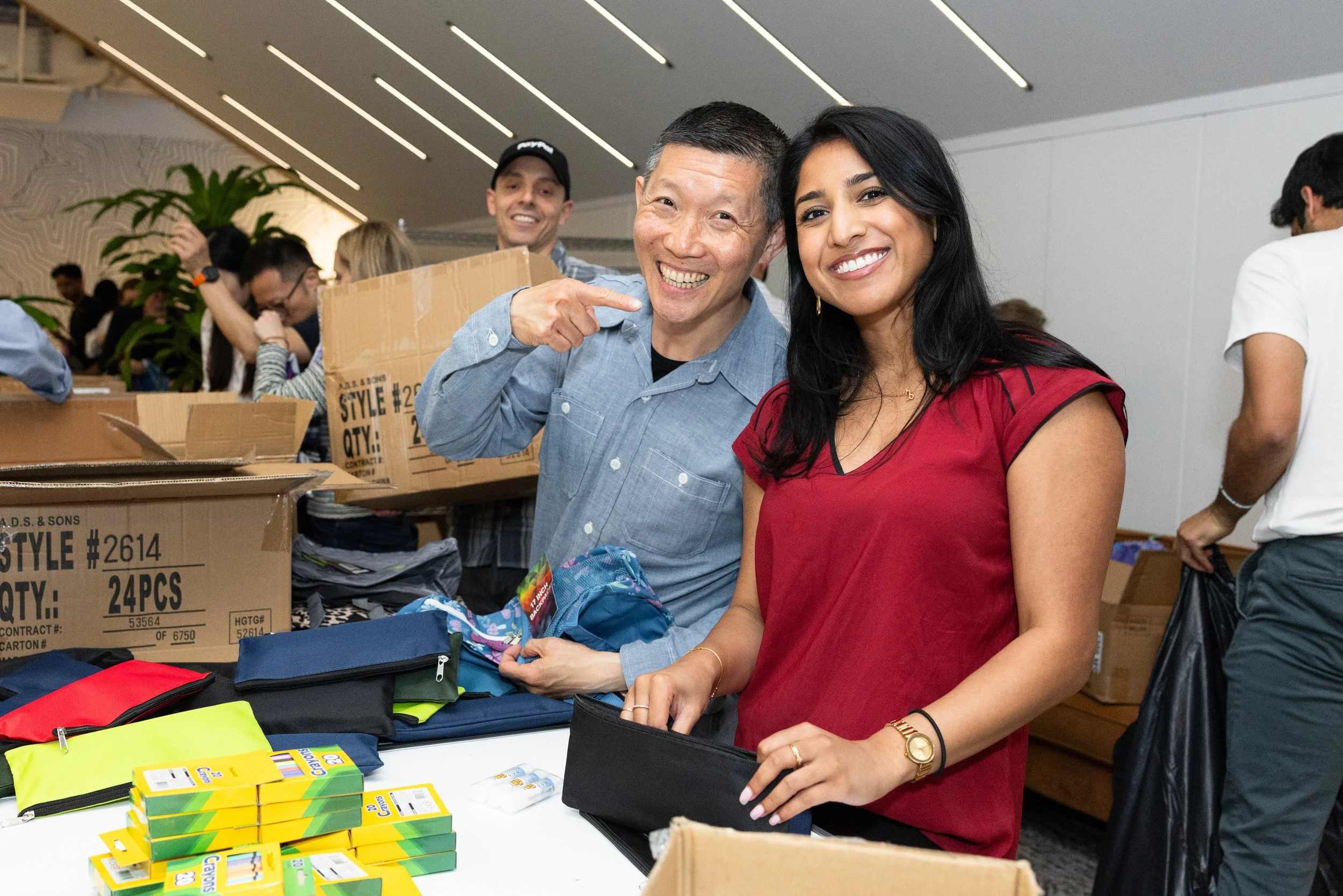A man and a woman smile at the camera in the midst of packing backpacks