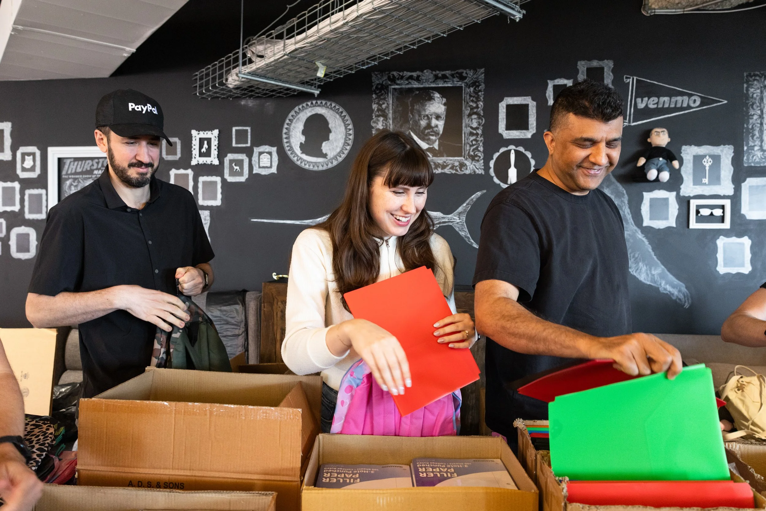 two men and a woman pulling out folders out of boxes at their offices as part of a corporate volunteer day