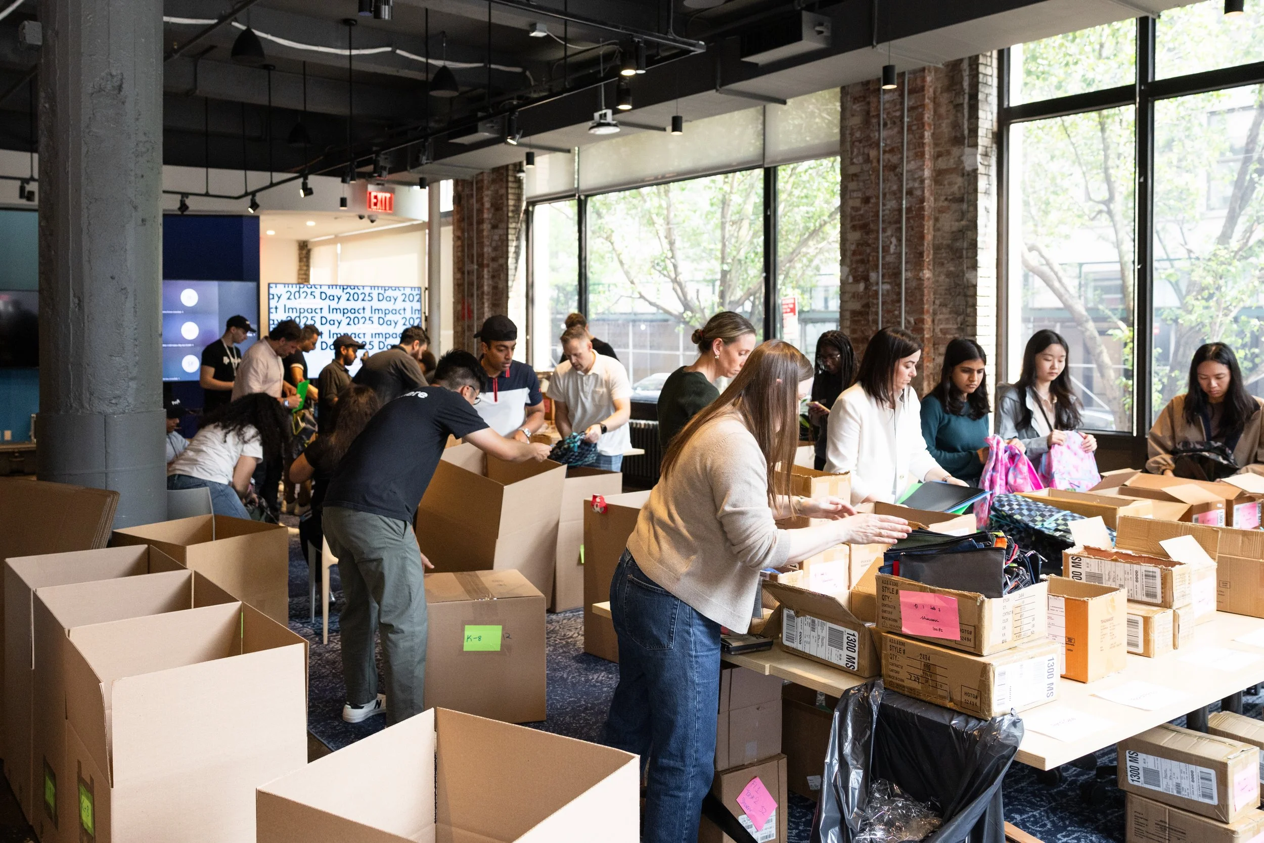A room full of corporate volunteers filling  backpacks with school supplies