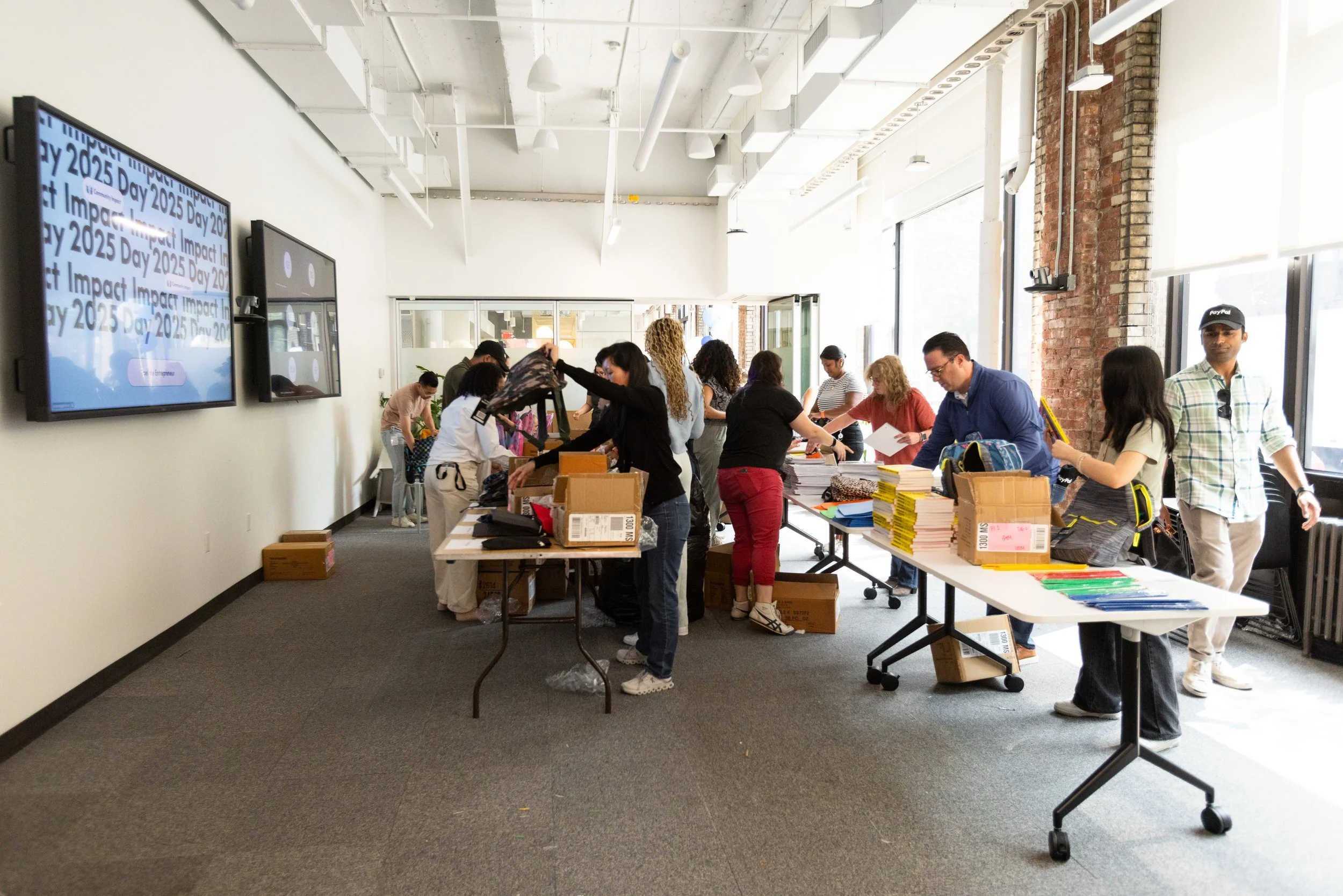 a room full of people stuffing backpacks with school supplies to distribute to a nonprofit