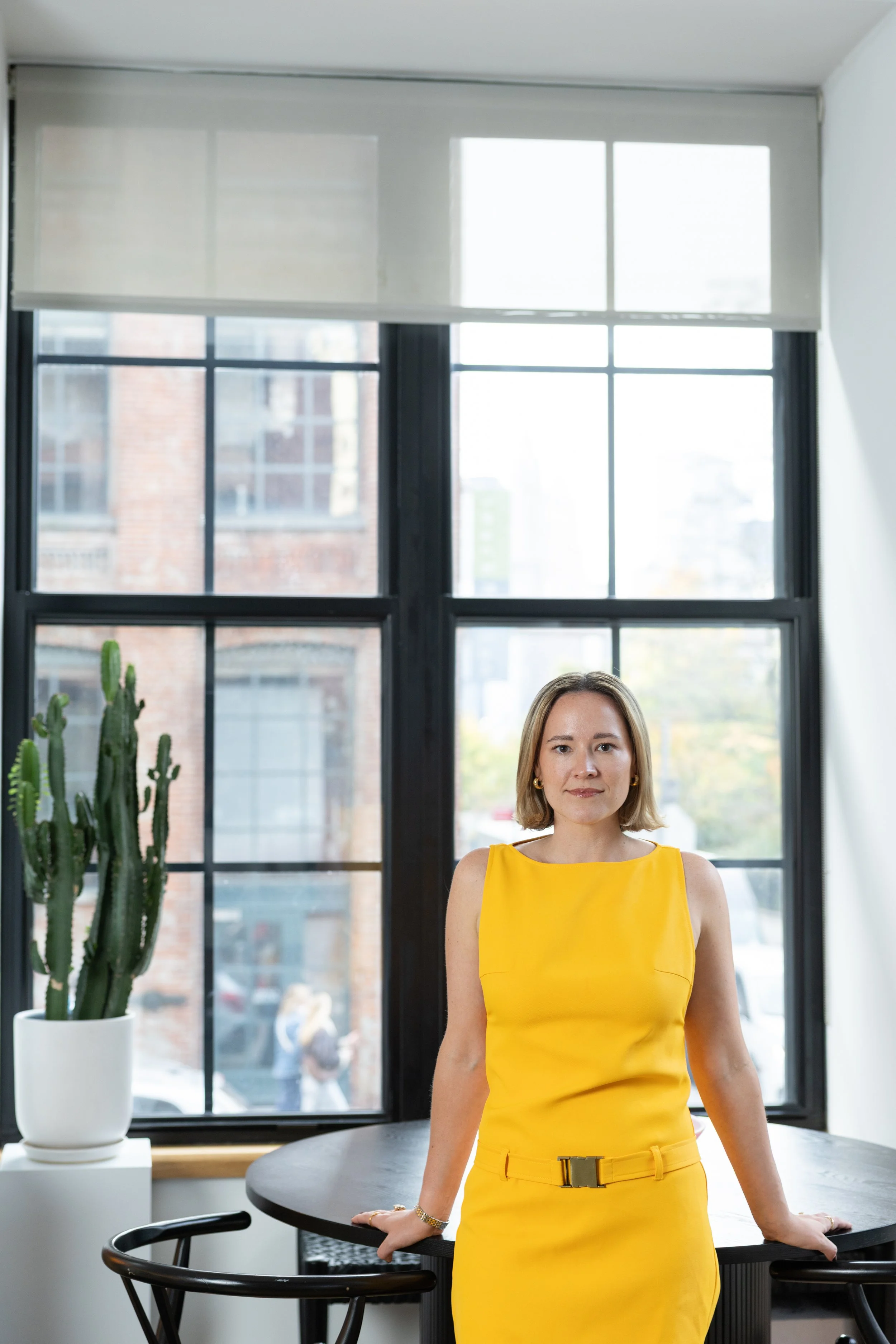 A woman in a yellow dress stands in front of a table in her DUMBO apartment 