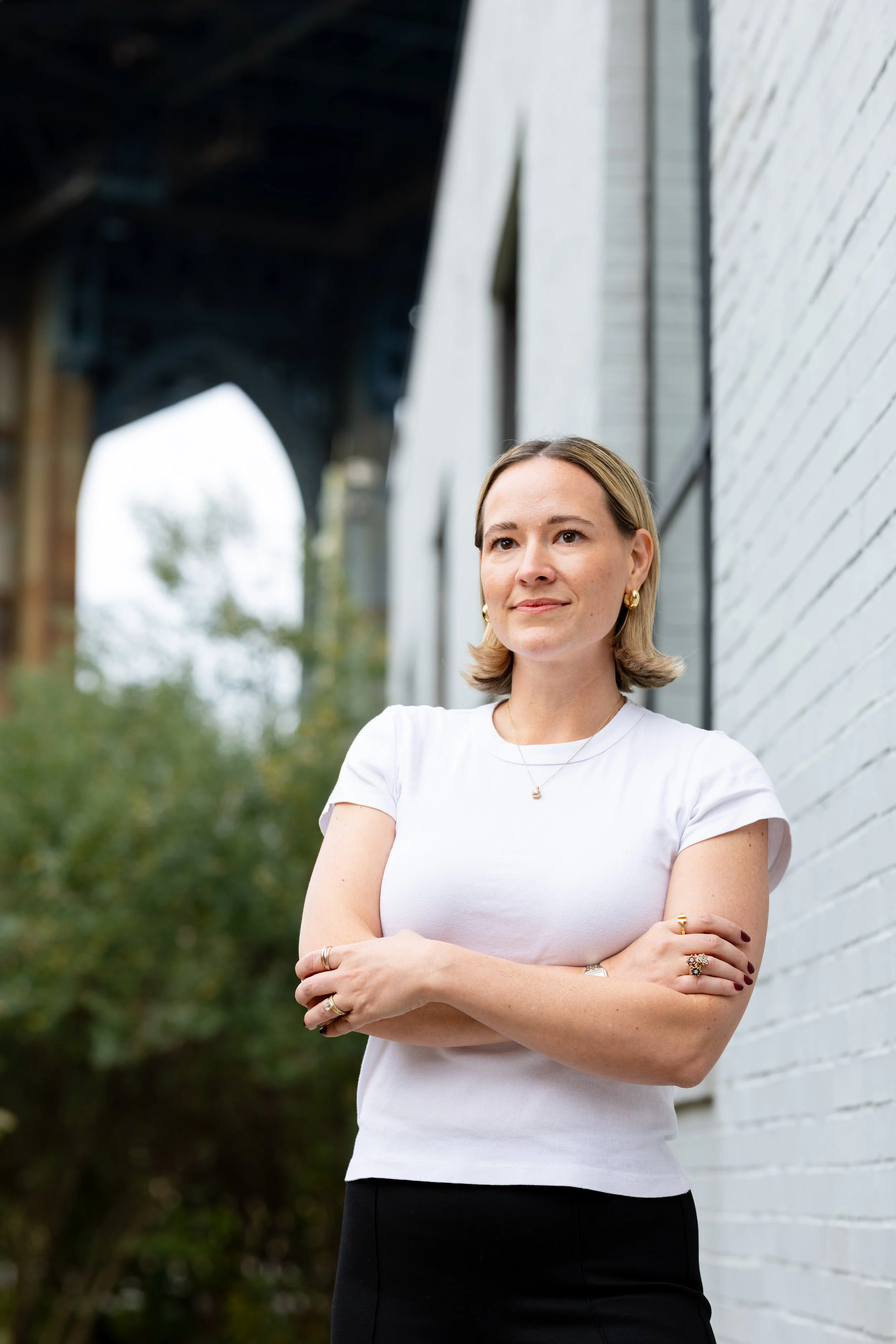 A woman with blond hair and a short sleeve t shirt stands in front of the Manhattan Bridge