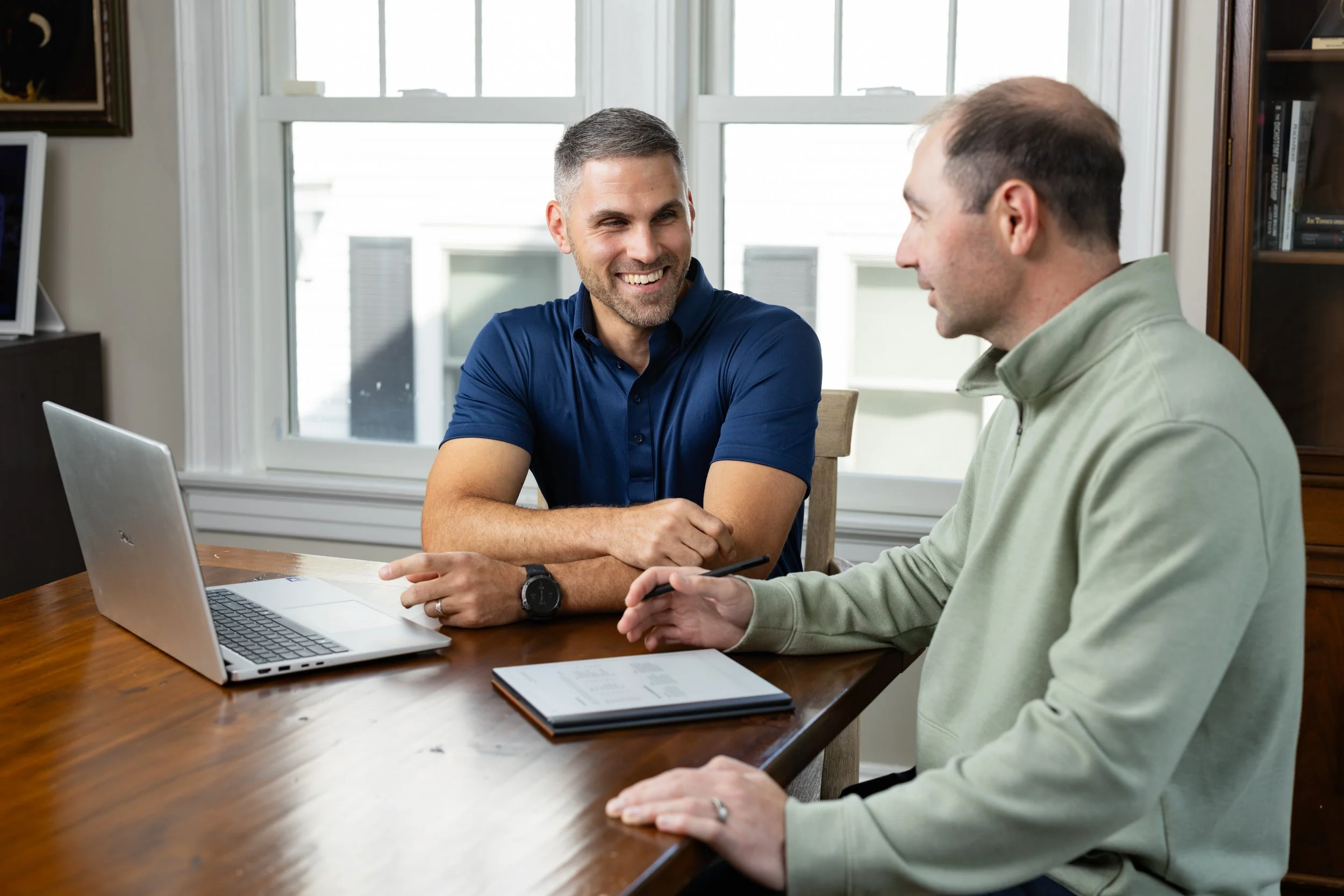 Two men at a conference table working with a laptop and notebook