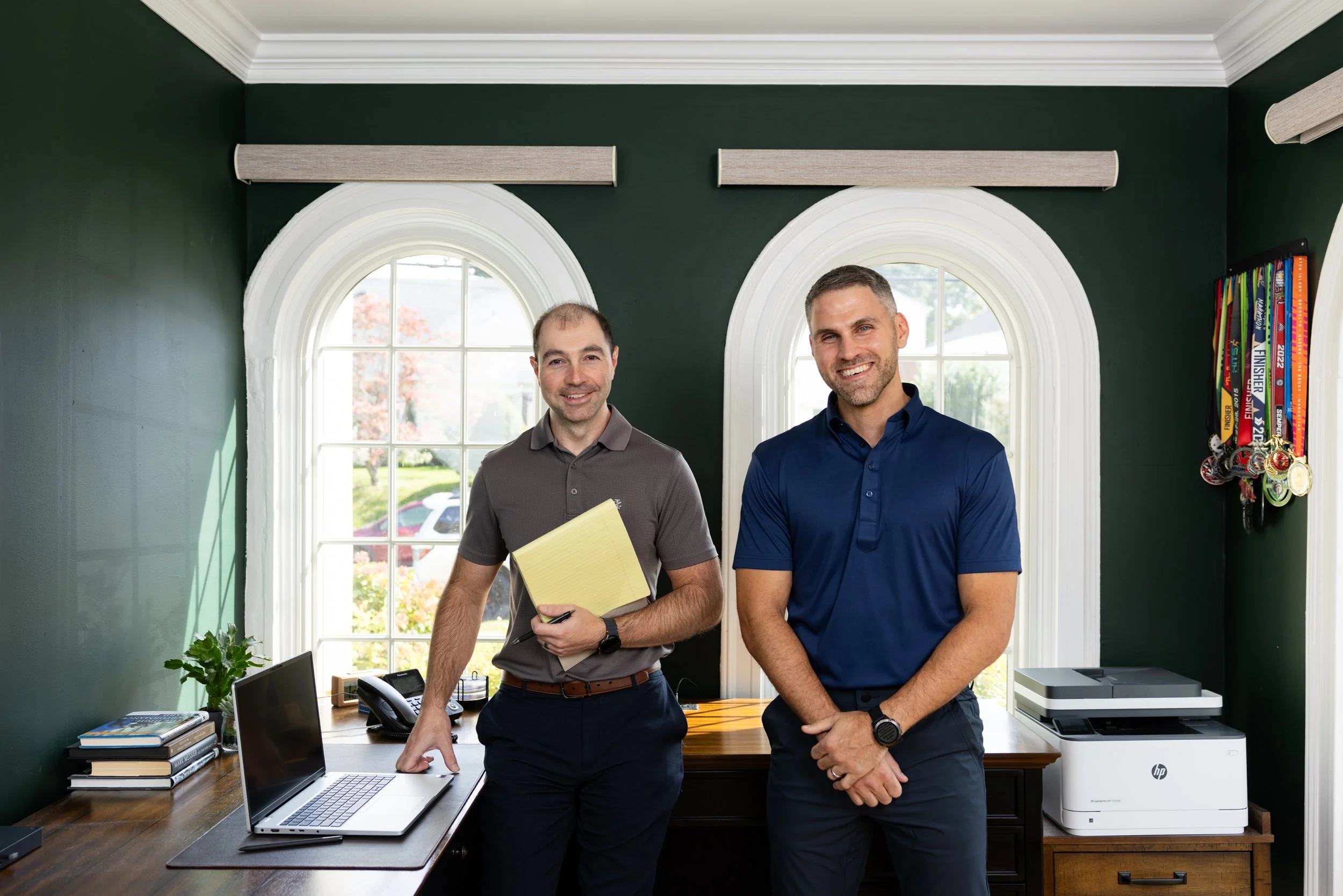 Team portrait depicting two men standing in front of a work desk smiling 