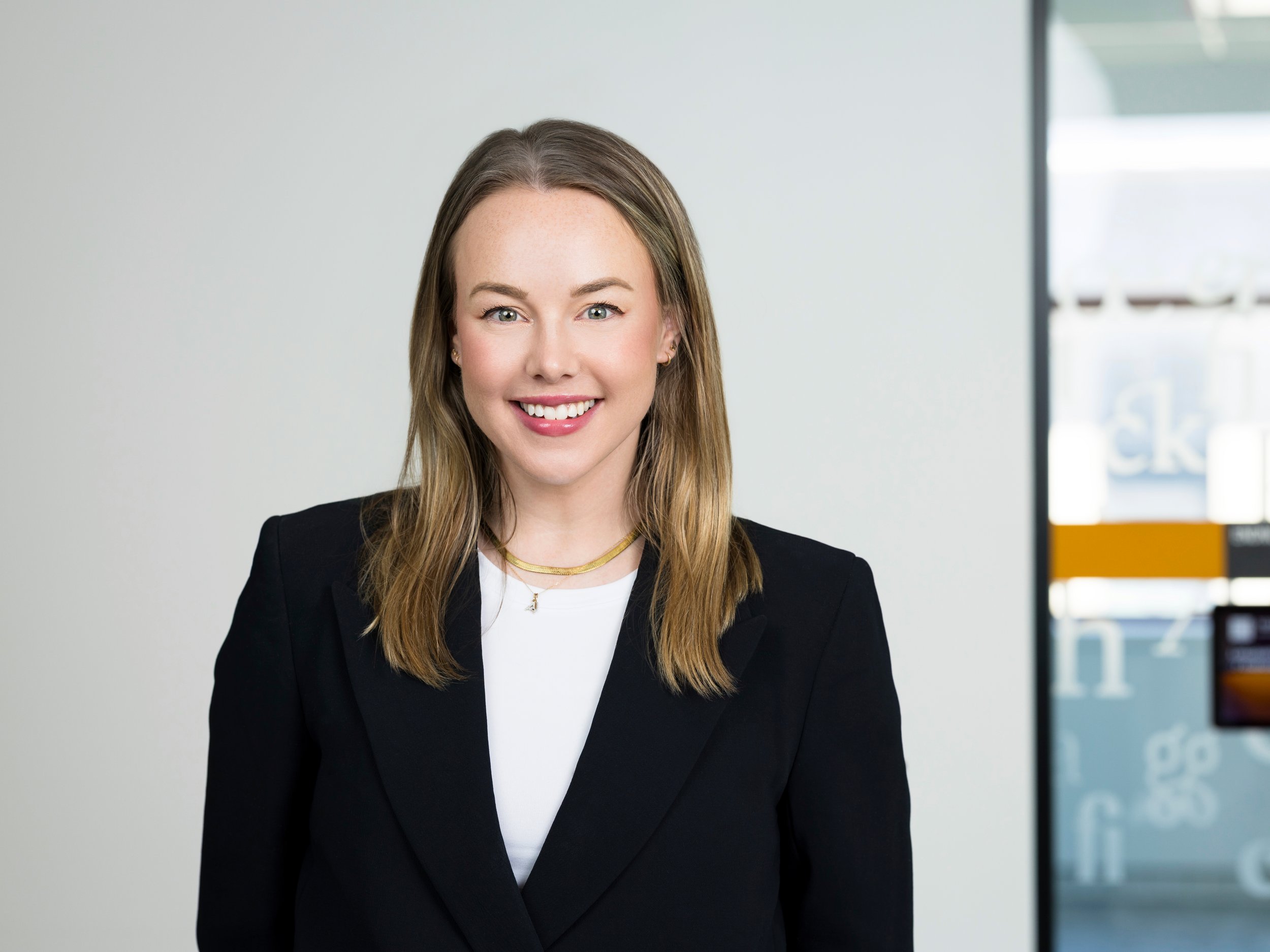 Headshot of a woman with long hair, white shirt, and black blazer in an office setting at LinkedIn