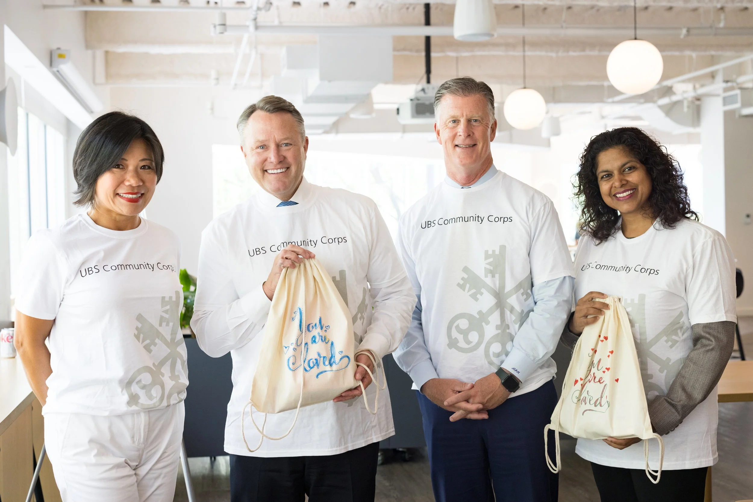 four corporate volunteers smiling at the camera during a volunteer day showing bags they packed