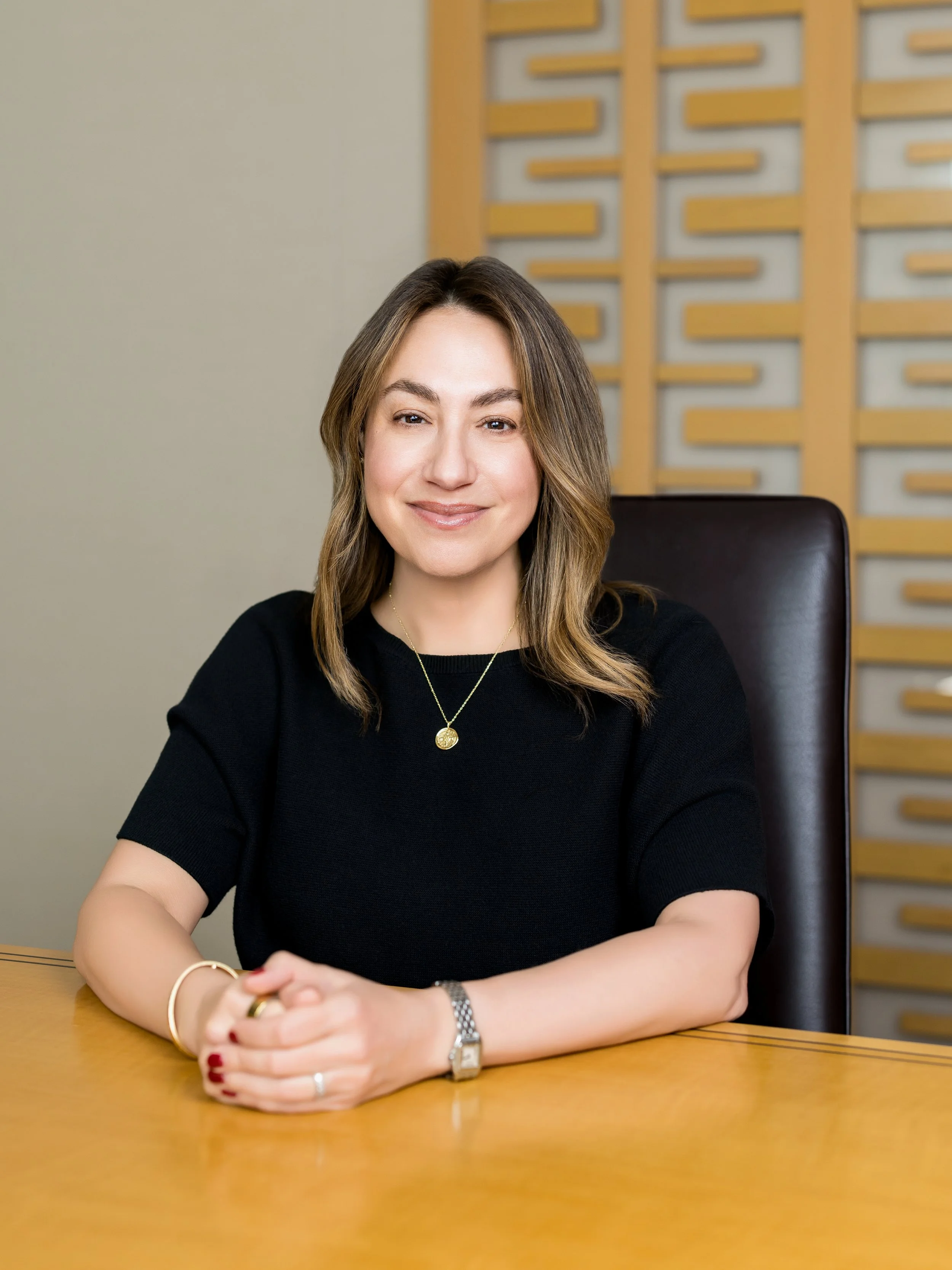 Woman with brown hair wearing a black shirt with a gold necklace seated at a conference table