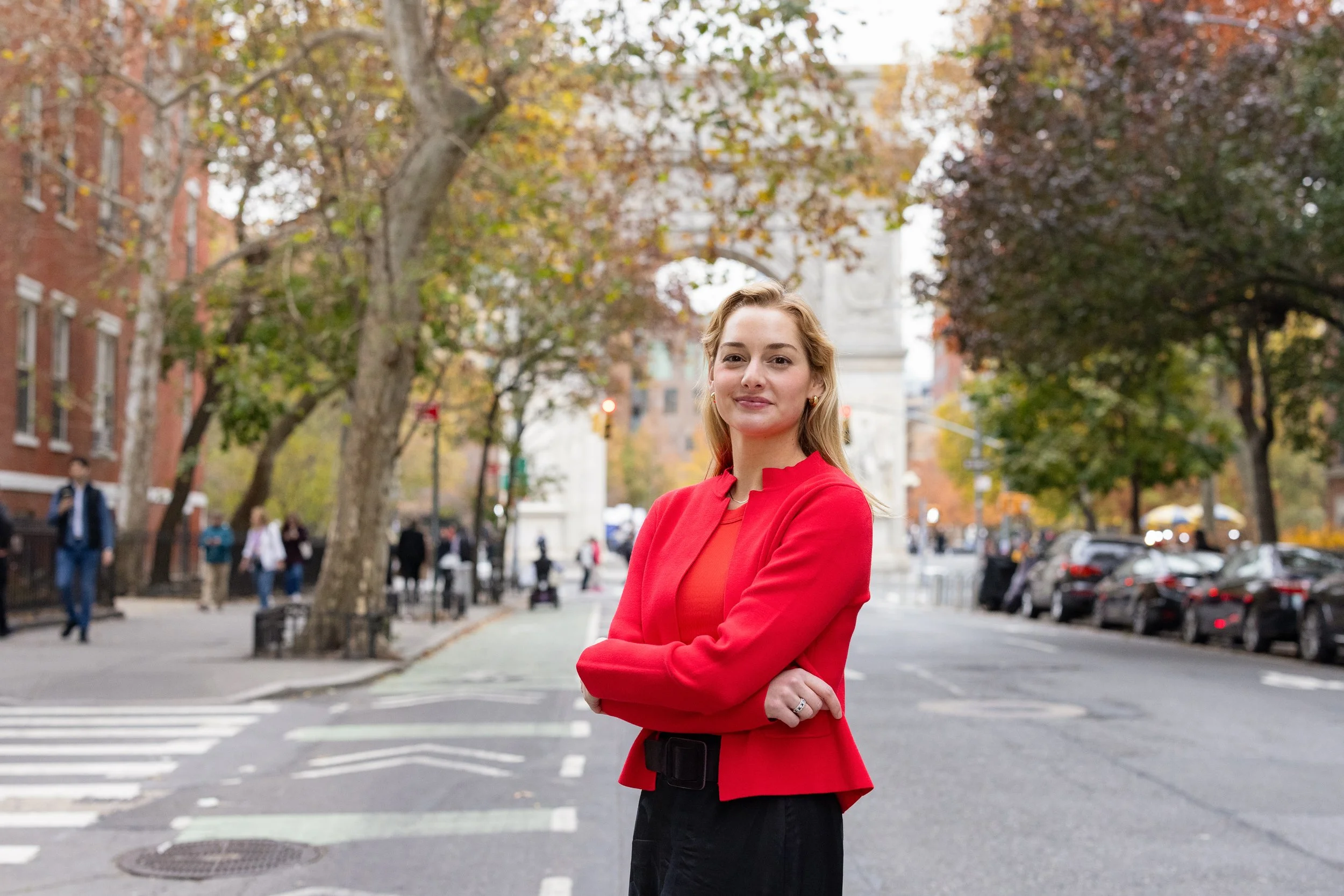 A woman with blond hair and a red sweater in front of Washington Square Park in New York