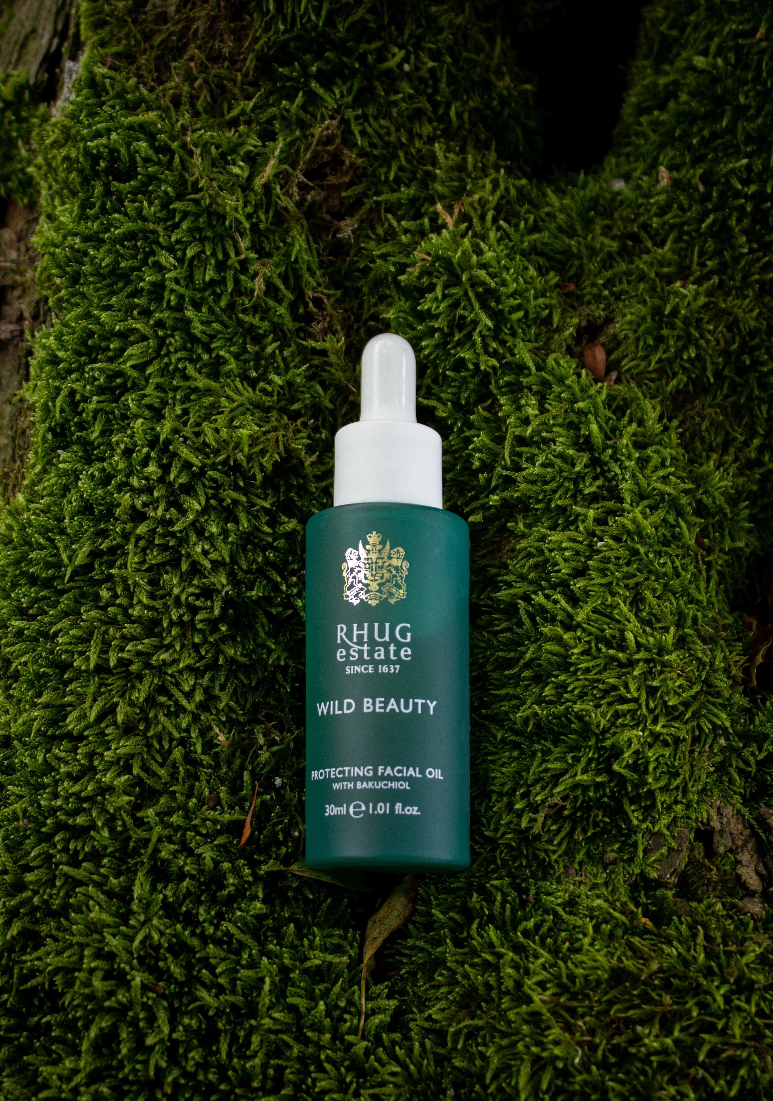 A bottle of Rhug Estate Wild Beauty facial oil with Bakuhiol is placed on green moss.