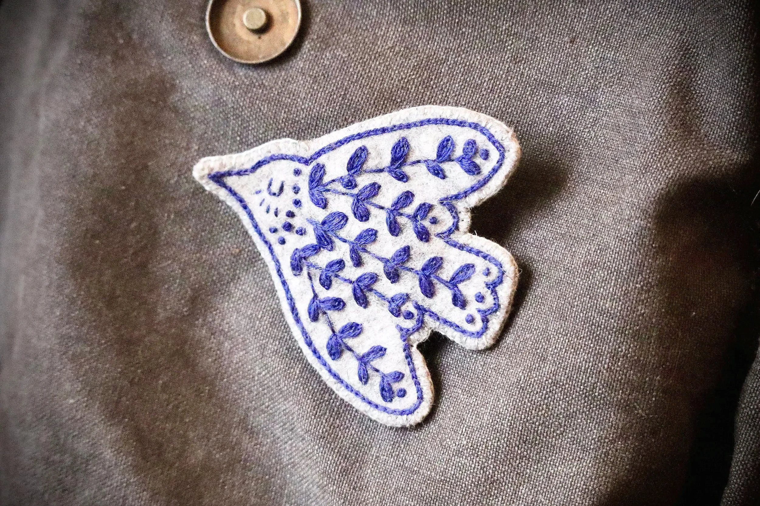 Close-up of a patch featuring a bunny with embroidered violet leaves and a dotted circle on a dark fabric background.