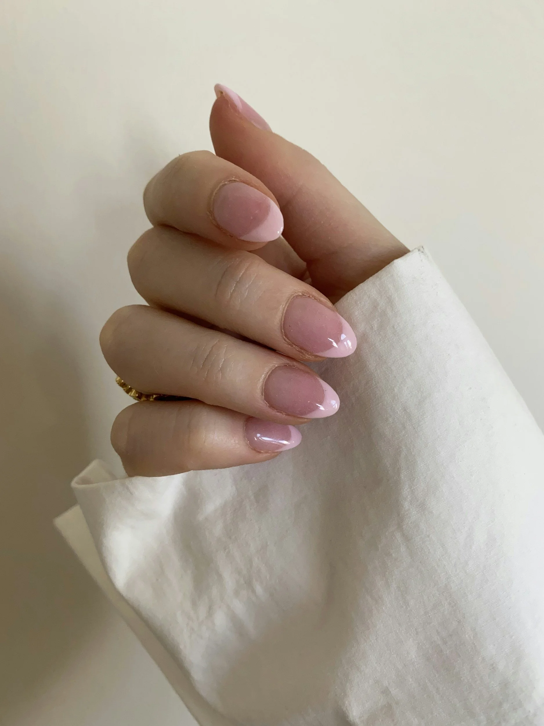 Close-up of a hand with manicured nails in a French style, holding a white cloth against a plain background.