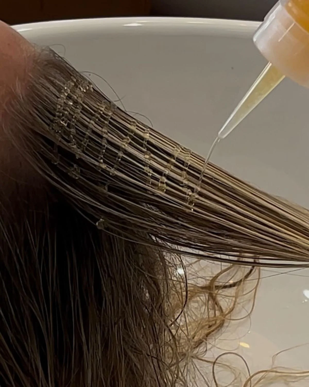 A person with wet hair getting a hair treatment with a liquid being applied to their scalp.