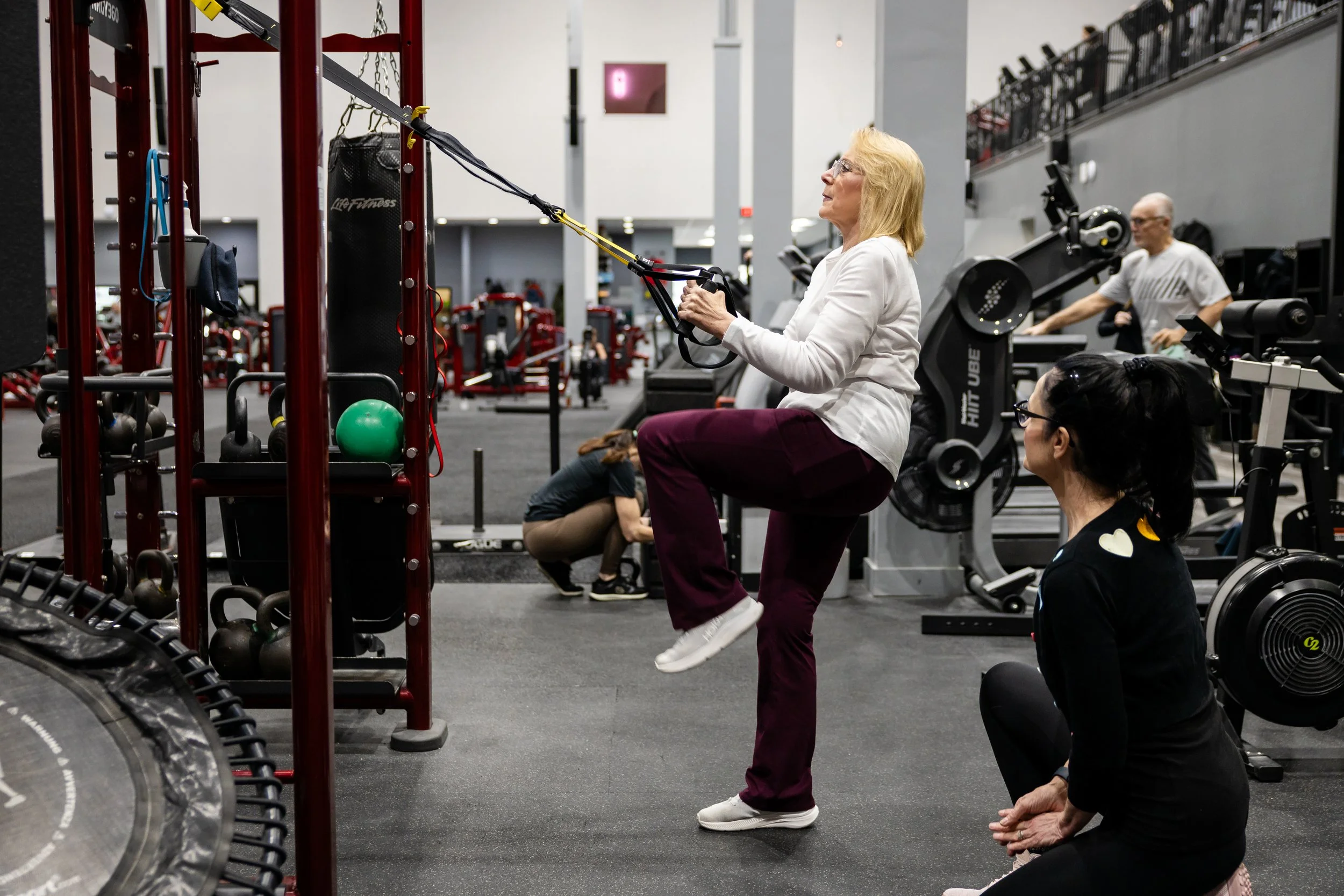 A man lifting dumbbells while seated on a bench in a gym with American flag hanging overhead.