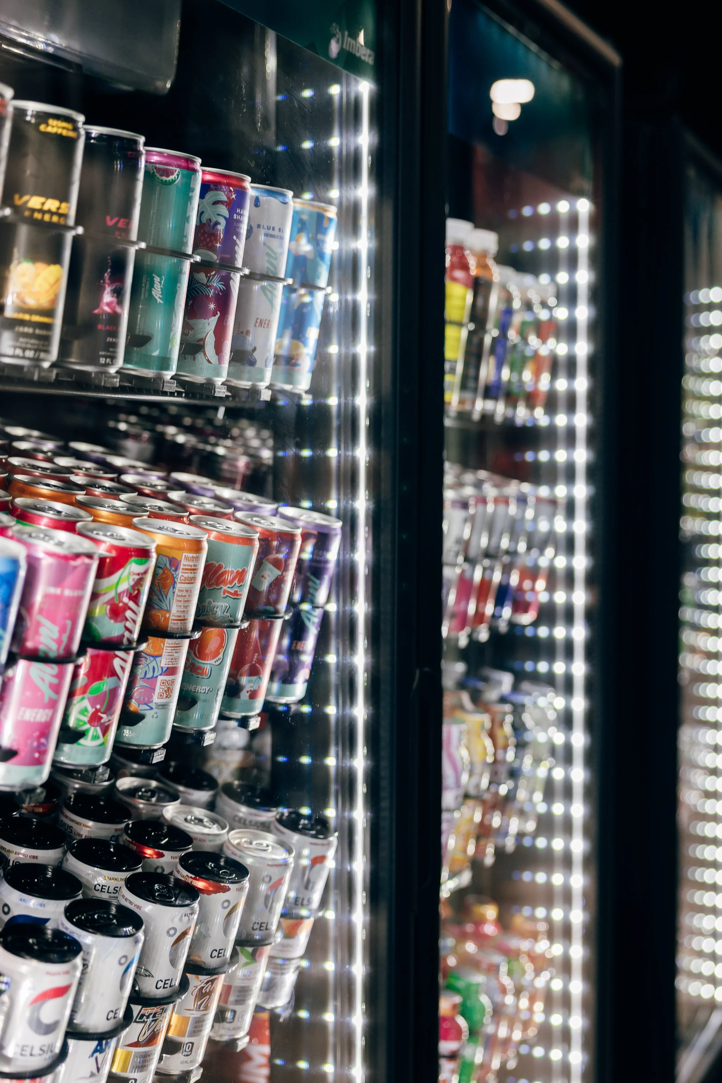 A vending machine stocked with various canned drinks, illuminated with bright white LED lights.