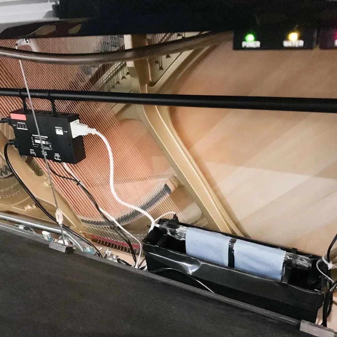 Innenansicht eines Klaviers mit sichtbaren Kabeln und elektronischer Ausstattung an der Seite.