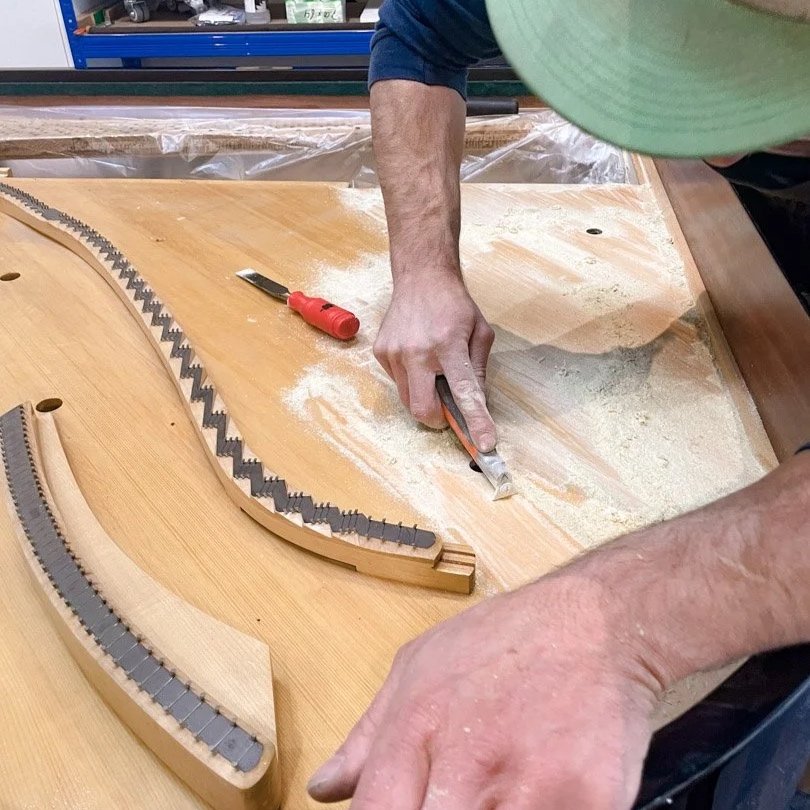 Ein Handwerker arbeitet an einem Klavier, schneidet Holzteile mit einem Cutter. Es liegen Werkzeuge auf dem Tisch.