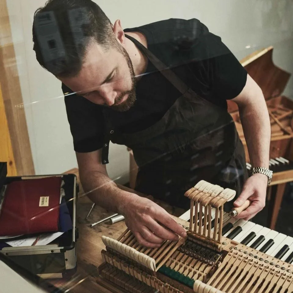 Stefan Blumer repariert das Innere eines alten Klaviers, sichtbar die Hämmer und Mechanik, während er die Stifte korrigiert.