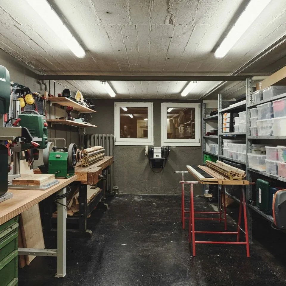 Werkstatt mit Werkzeugmaschinen, Regalen mit Kunststoffboxen und einem Tisch mit einem zusammengebauten Klavier.