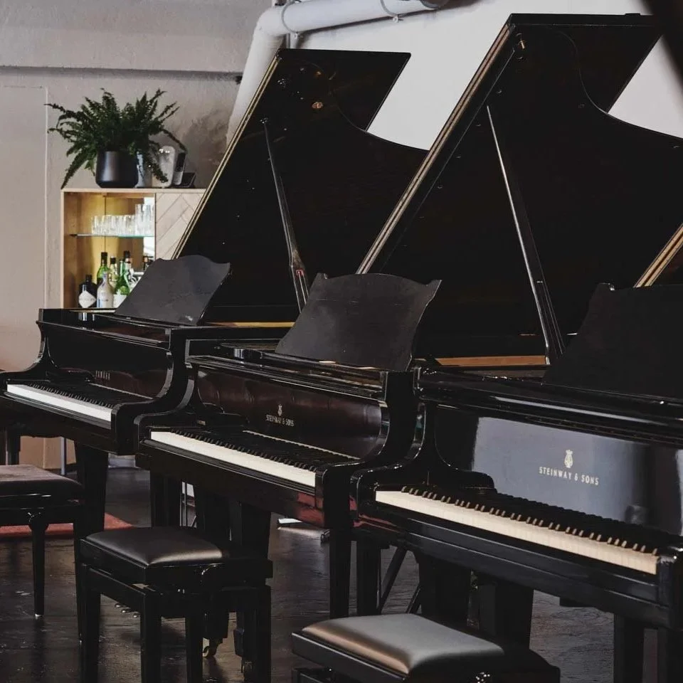Zwei Flügelpianos, eines von Steinway & Sons, in einem Raum mit Stühlen davor.